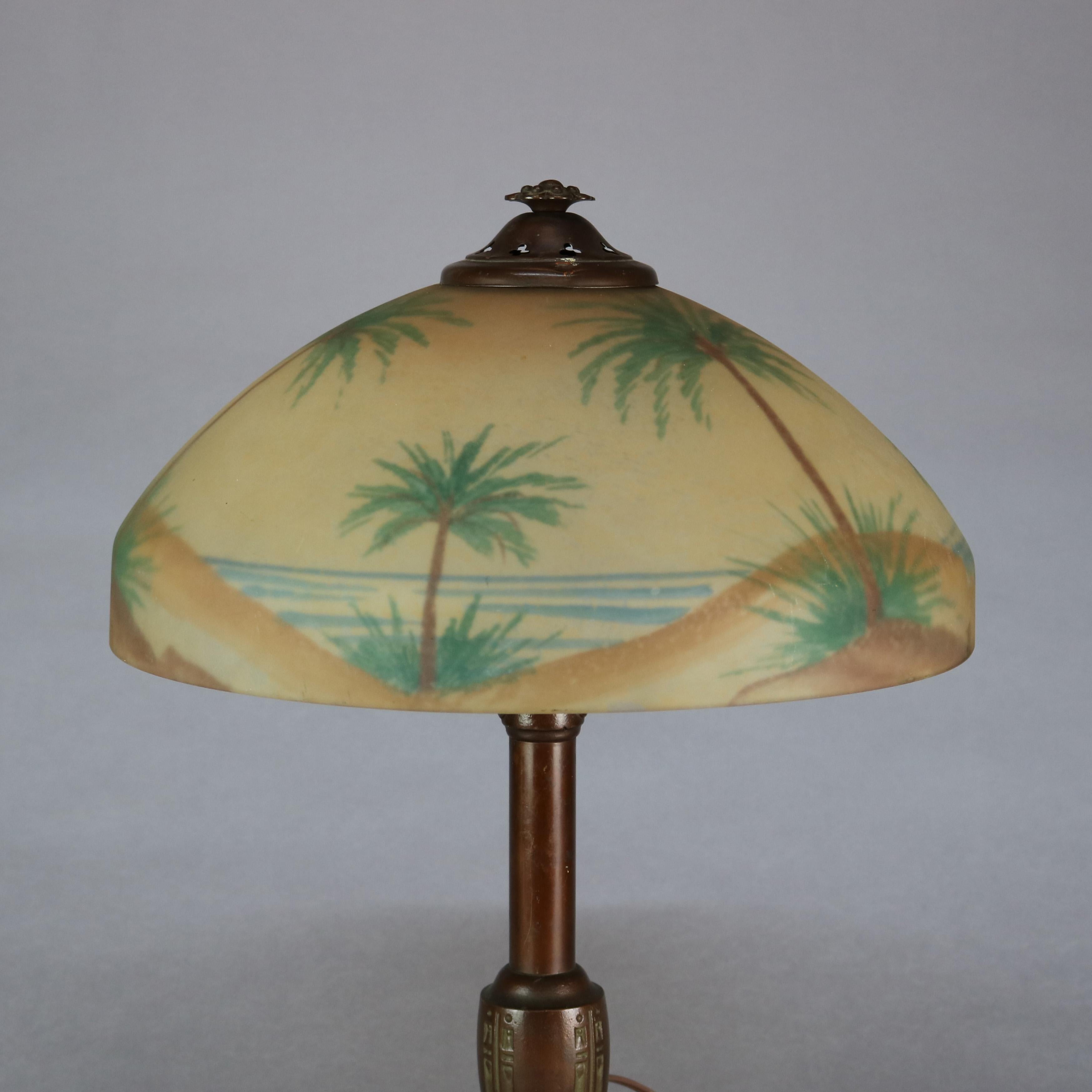 An antique table lamp in the manner of Pittsburgh Lamp Co. offers dual socket foliate cast base with foliate and scroll embossed base surmounted by shade having reverse hand painted glass dome with beach seashore scene with sunset, sand dunes,