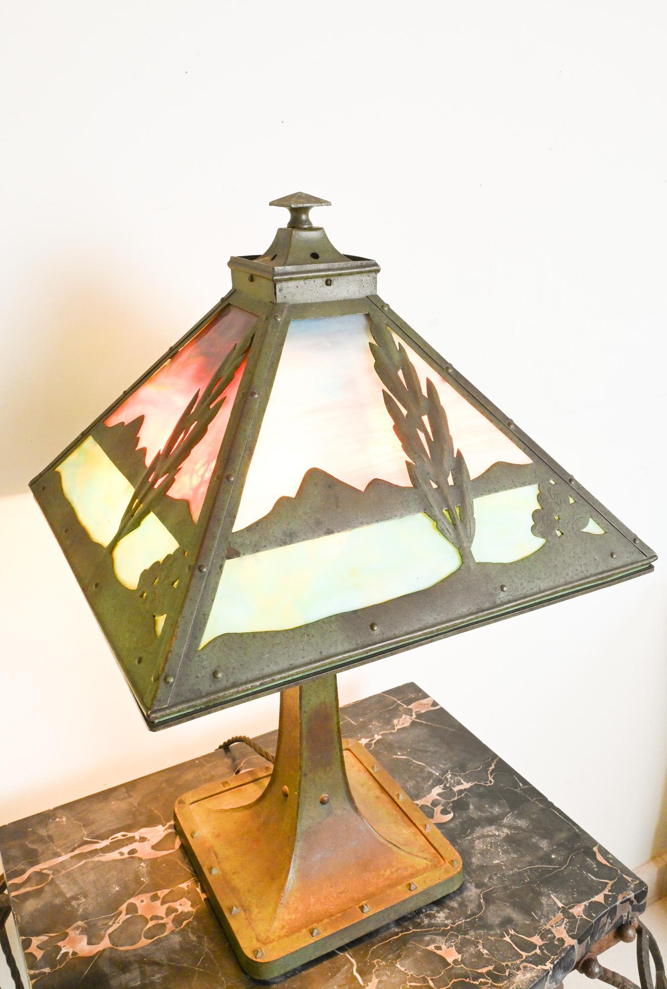 Un rare exemple d'éclairage américain du début du 20e siècle, attribué à Pittsburgh Lamp, Brass & Glass Co. L'abat-jour pyramidal, riveté à la main, comporte des panneaux de verre de scories richement colorés et une silhouette d'arbre et de
