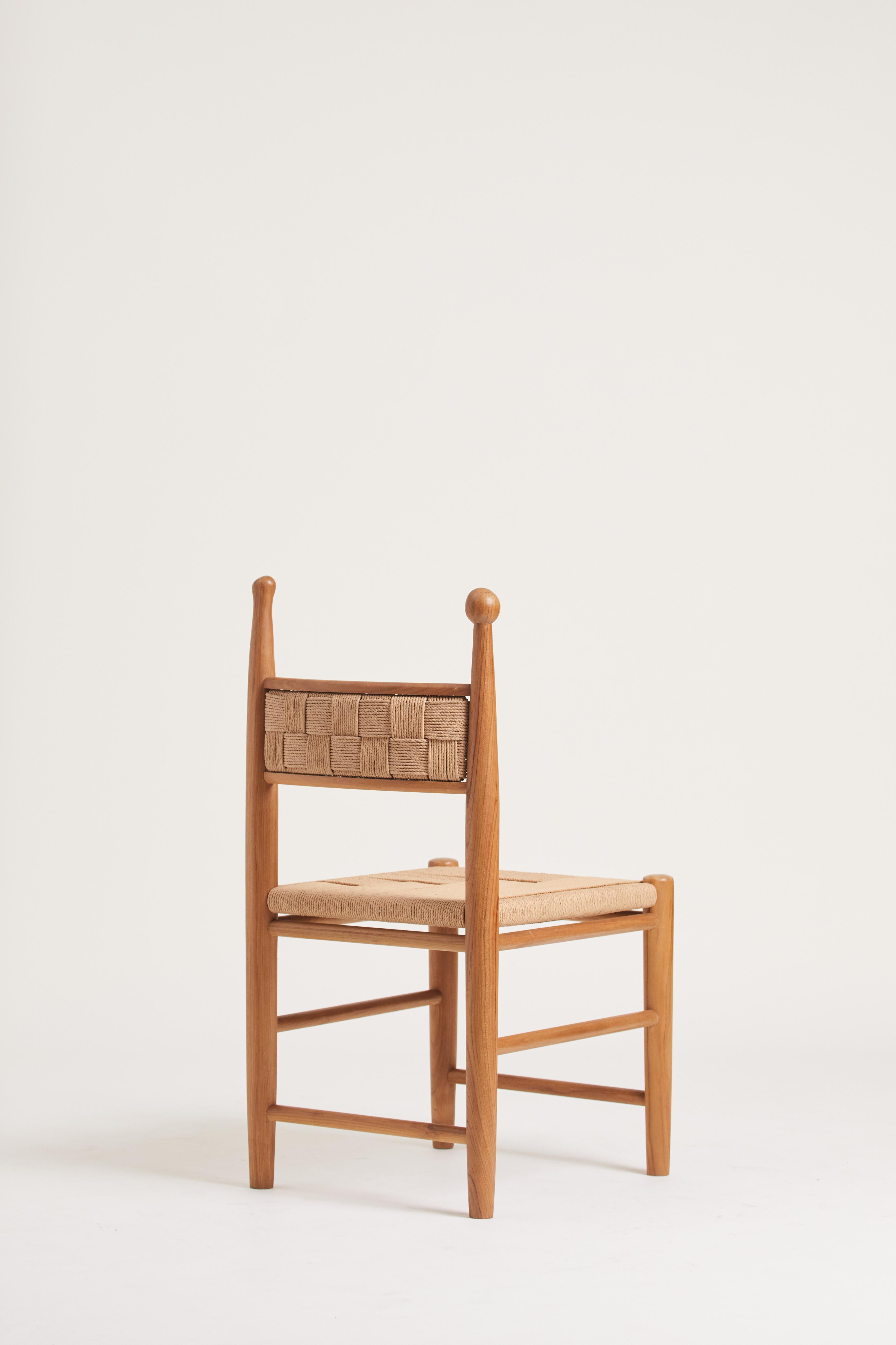 The Pitufi Dining Chair in its low-back version is a simplified piece featuring a solid teak wood frame. Characterized by its upright and elegant backrest, it incorporates two uniform grids of braided loom that connect to a similarly woven seat. The