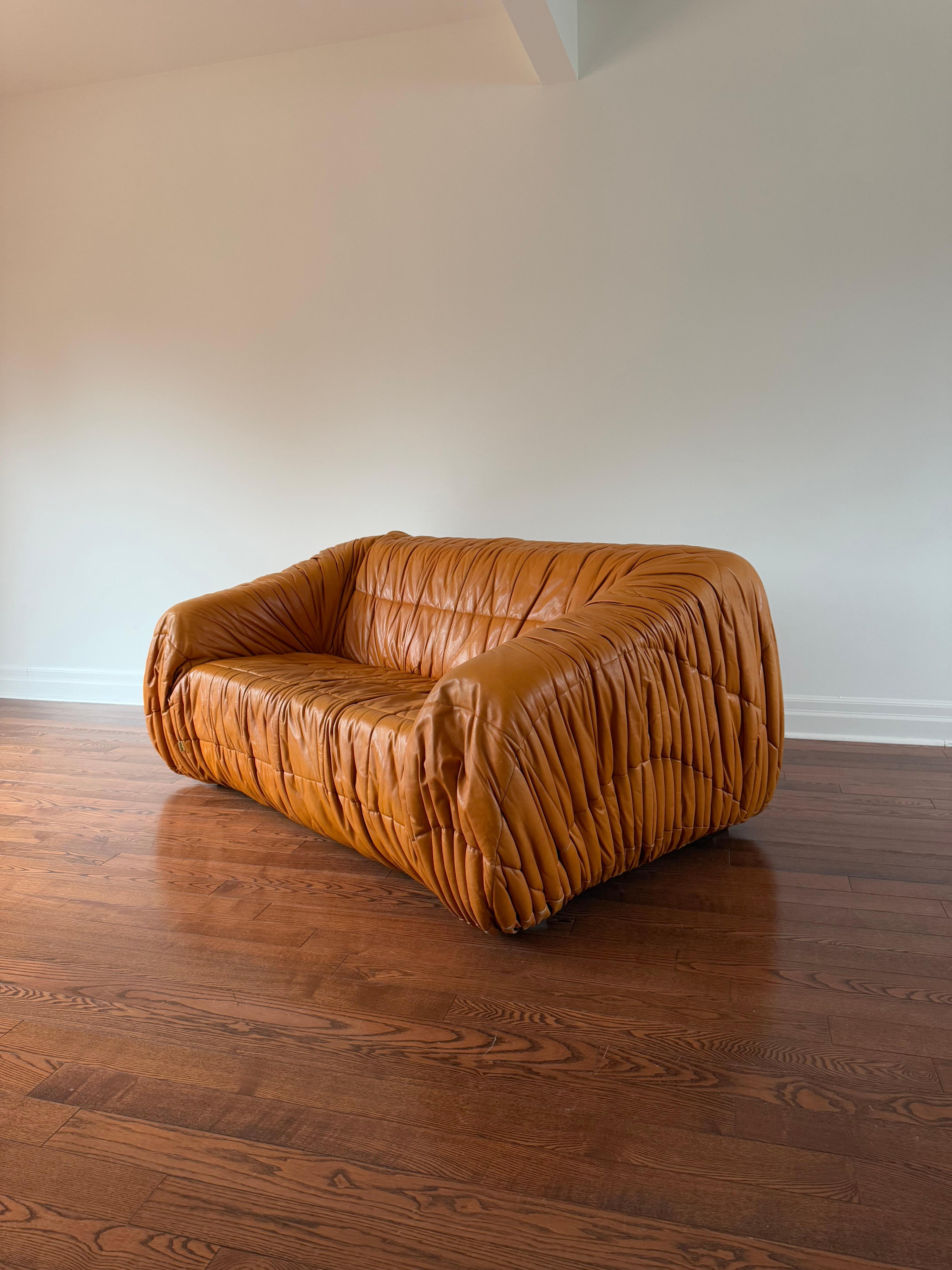 Loveseat Piumino en tapicería original de cuero plisado. Tanto la estructura de espuma como la piel están en muy buen estado. Etiqueta original presente en la parte delantera derecha del sofá [en la foto].

Icónico y raro diseño italiano de los