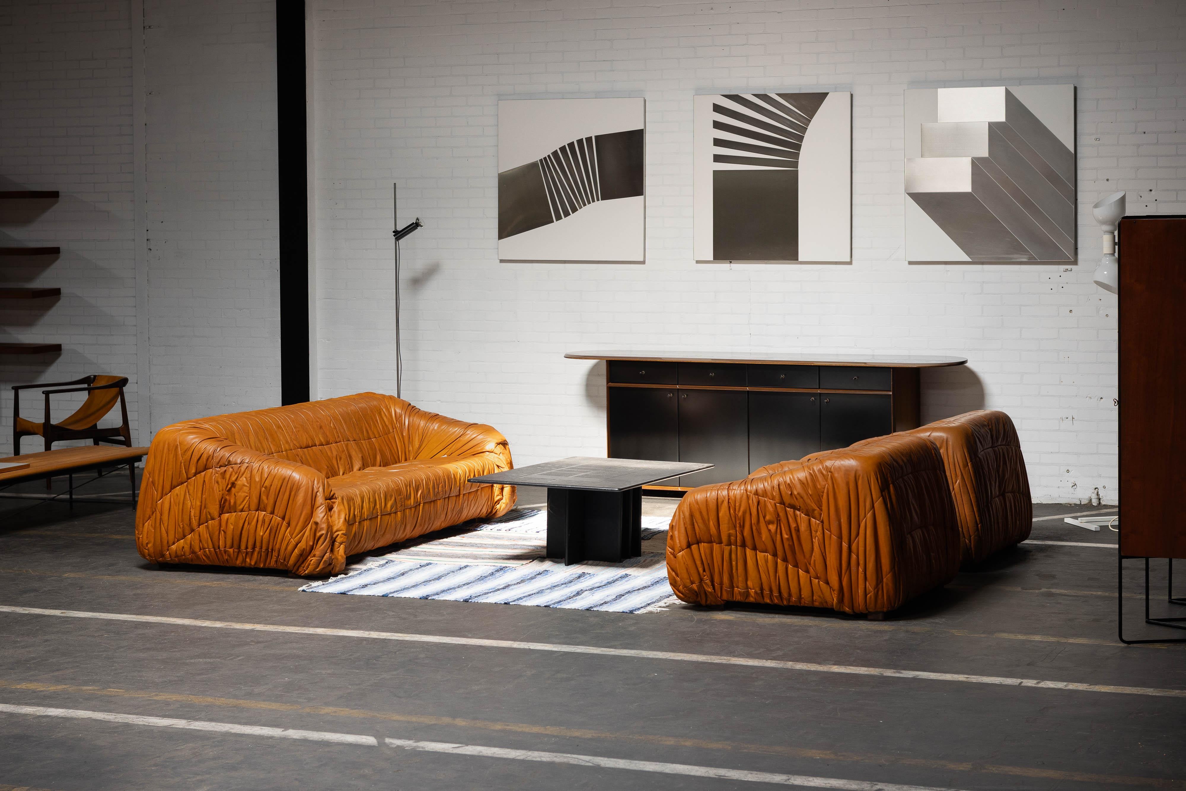 Il divano Piumino, disegnato dal rinomato trio De Pas, D'Urbino e Lomazzi e realizzato da Dall'Oca in Italia nel 1970, è un mix perfetto di design giocoso ed eleganza senza tempo. Il lussuoso rivestimento in pelle cognac del divano presenta una