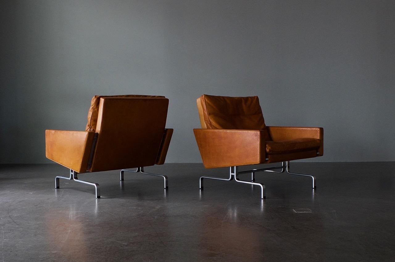 The PK 31 is a true design icon. Pair of lounge chairs PK 31, in original cognac leather. Matt, chrome-plated spring steel frame with wood-framed panels and down-filled cushions in leather. Designed by Poul Kjaerholm in 1958, and produced by E. Kold