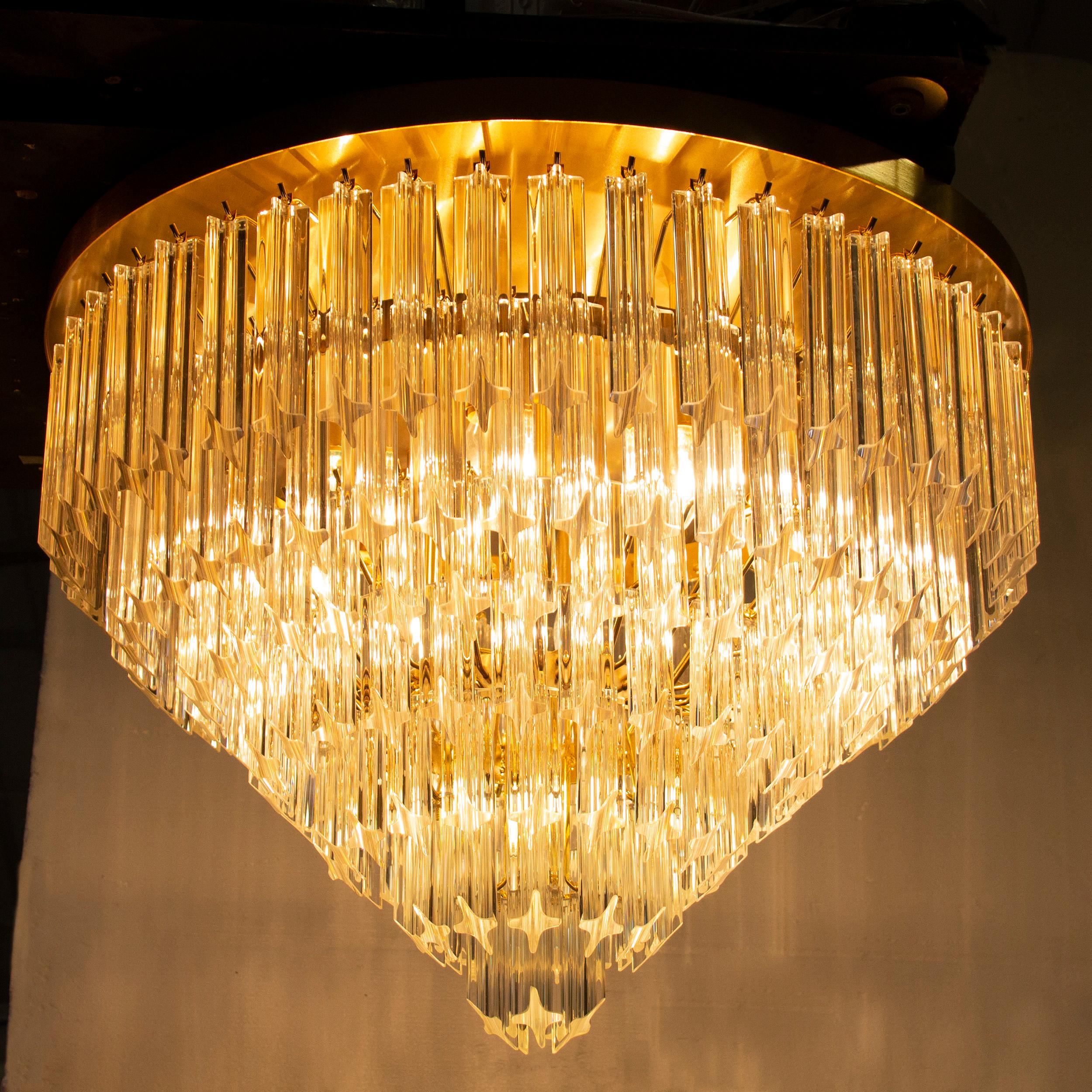 Grande lampadario plafoniera con triedri o quadriedri in vetro di Murano ispirato al mid-century italiano.

Direttamente dalla fonte:
Non siamo semplici rivenditori, ma produttori diretti! Situati vicino a Venezia, nel cuore dell'industria vetraria