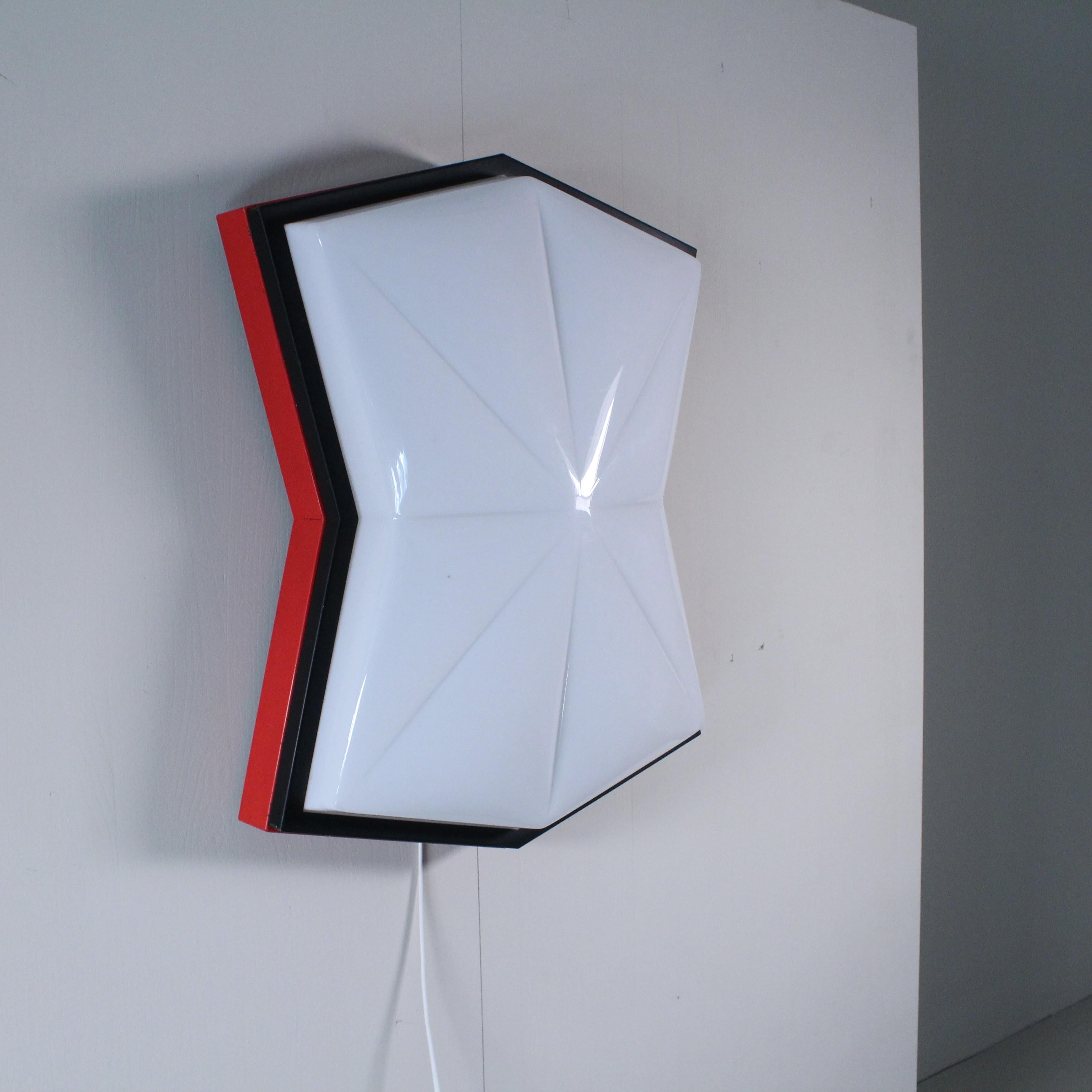 This Space Age-style ceiling light is an example of iconic 1980s design, with its mix of bold geometric shapes and innovative materials. The structure is composed of bright red painted metal and white plastic, combined to create a striking visual