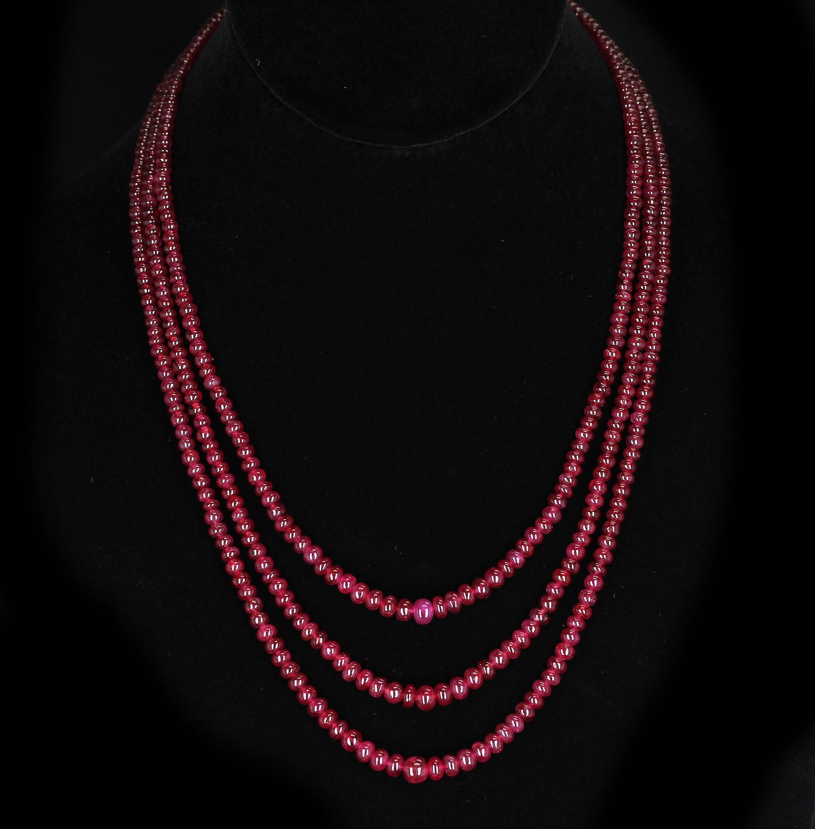 Eine Halskette, bestehend aus drei Strängen mit glatten und schlichten Rubinperlen. Die Länge reicht von 17