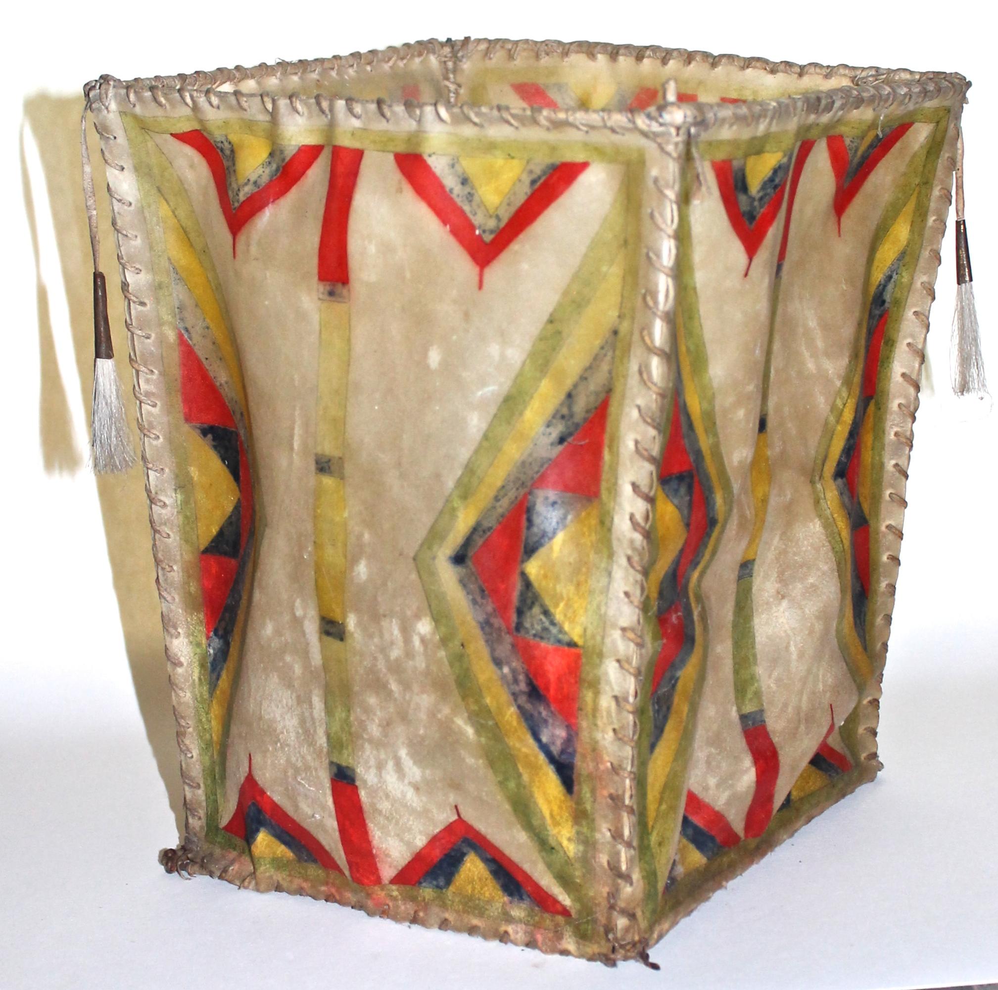 An open truncated basket constructed of wire with rawhide sides, painted with geometric motifs in natural paints. Tassels, held with brass.