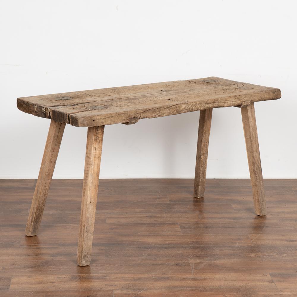 This rustic plank top console table with splay peg legs originally served as a work table.
The top reveals generations of use in the heavy gouges, cracks, stains and age related separation of the two heavy planks which add character and intrigue to