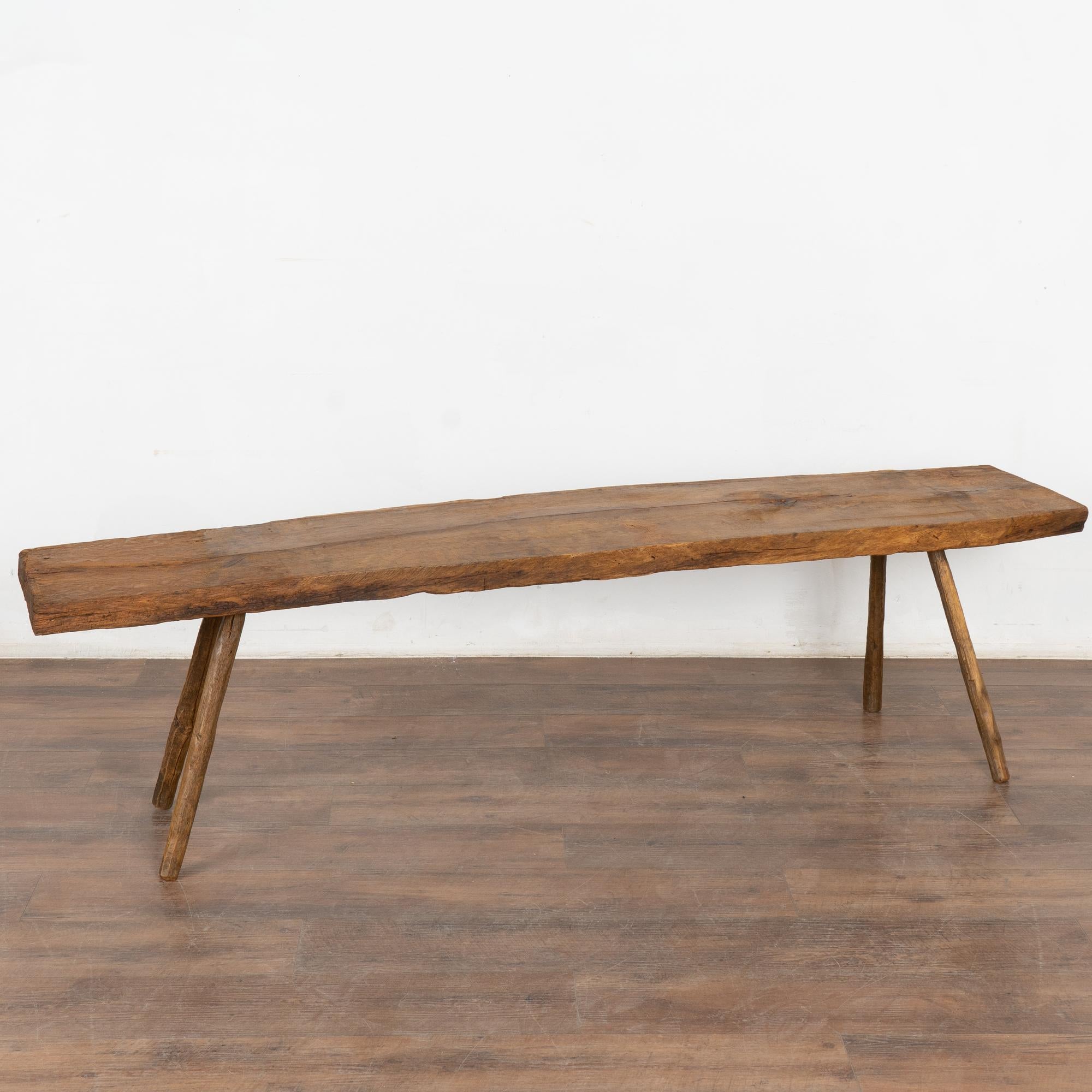 Rustic plank top bench with splay peg legs at 6.5' long.
The top reveals generations of use with cracks, nicks, stains and uneven ends which add a raw, organic feel to the narrow bench. 
Restored and waxed, this bench is strong, stable and ready for
