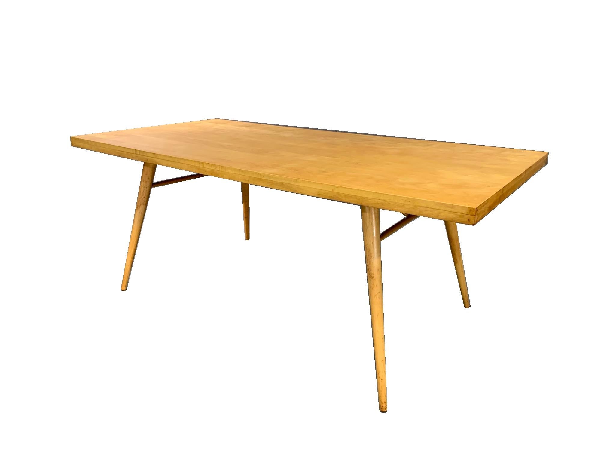 A satin clear coat finished solid maple McCobb dining table with active wood grain and gracefully splayed conical legs from Paul McCobb's Planner Group Collection for the Winchendon Furniture Company. Bright blonde wood table designed in simple,