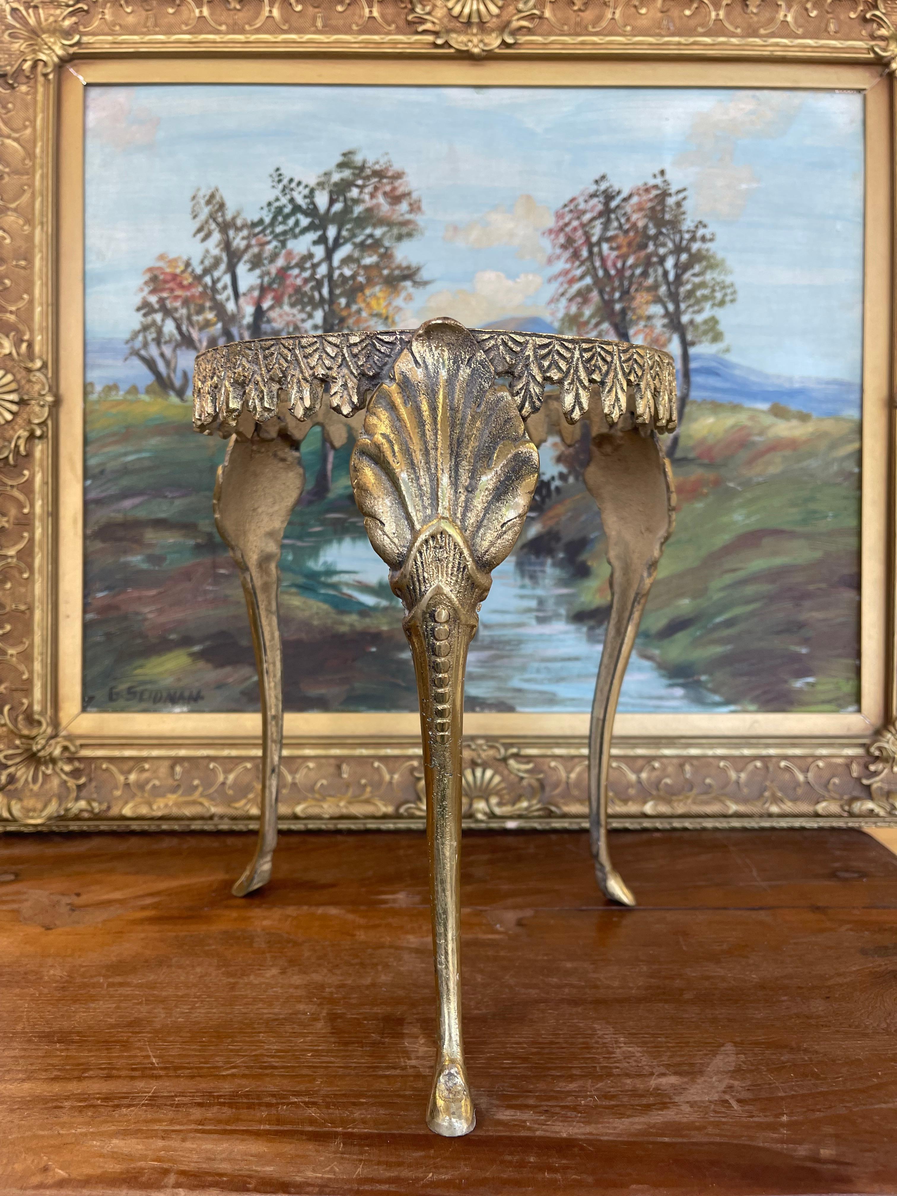 A plant stand featuring ornate decorative details and elegant cabriole legs. The upper ring is encircled with a relief of cascading leaf motifs, while each leg is adorned with shell-inspired embellishments and subtle beading. The three splayed legs