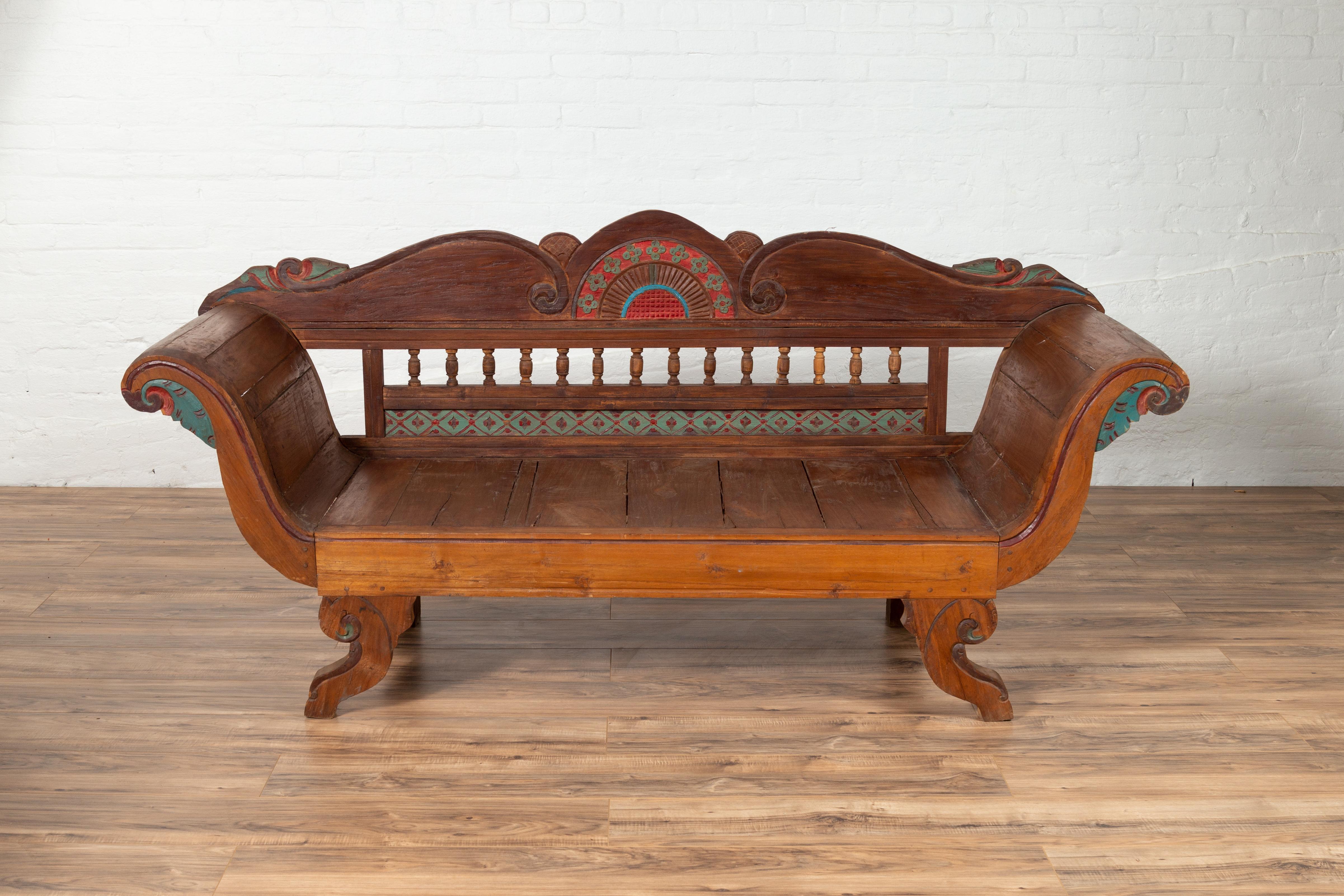 An antique Javanese teak wood plantation settee from the early 20th century, with hand painted décor, carved volutes and out-scrolling arms. Born in Java during the early 20th century, this exquisite teak wood settee can sit three people. Our eye is