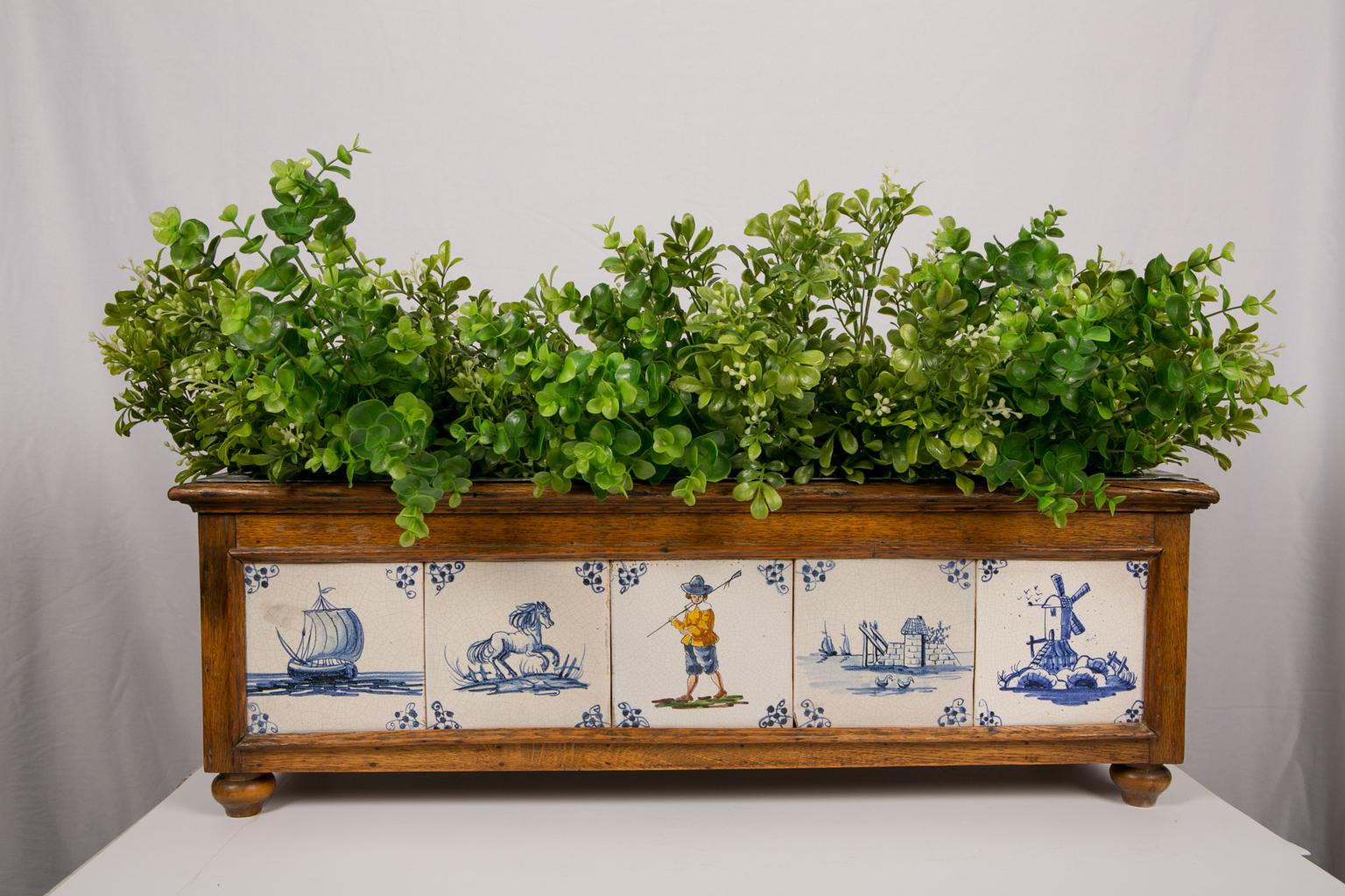 18th century Dutch delft tiles set in a modern planter. The wood planter is fitted with a tin liner and decorated with eight Dutch delft tiles.
The blue and white delft tiles show a galloping horse, a waterside scene, a sailing ship, a horse and
