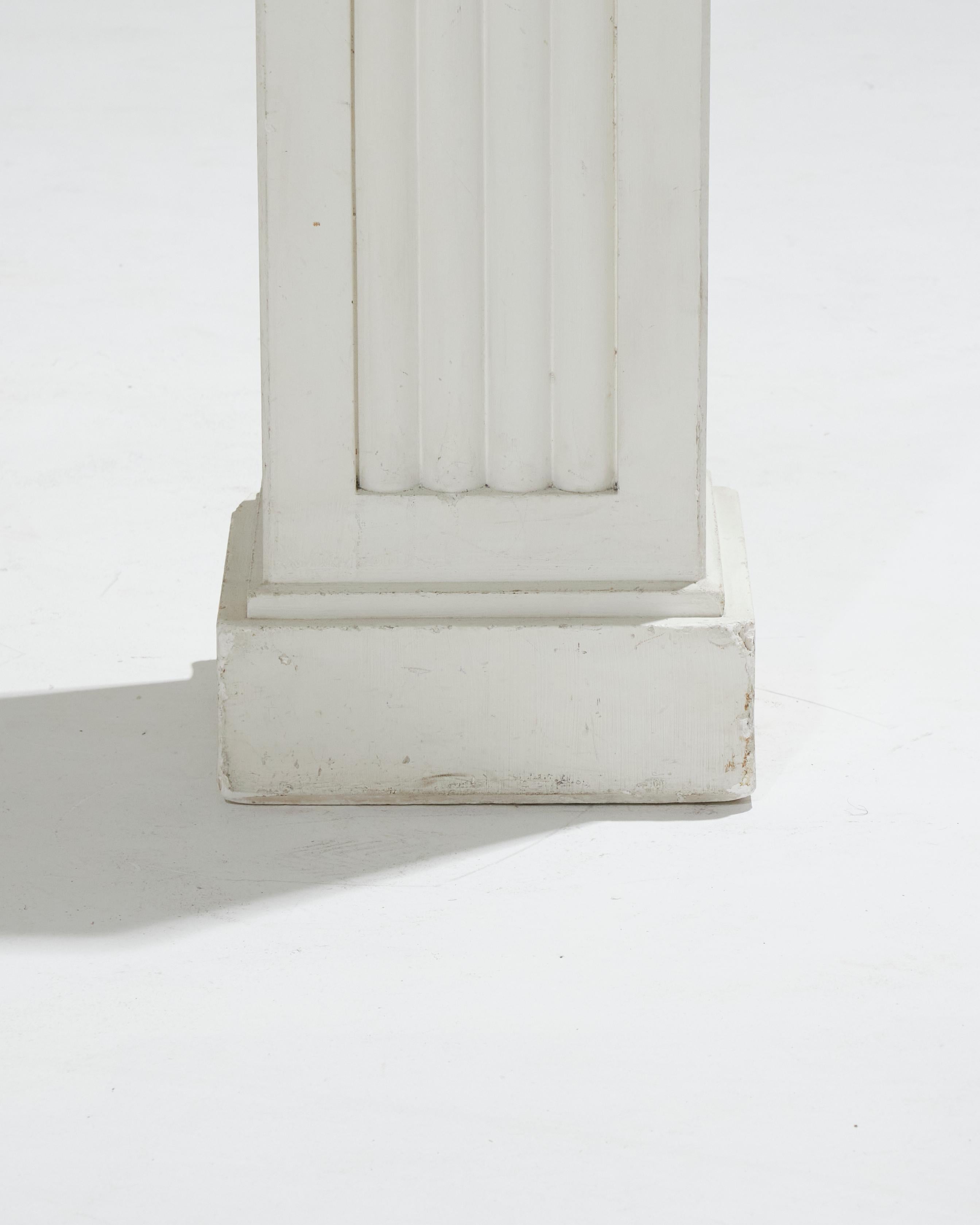 Colonne quadrangulaire en plâtre blanc, datant des années 1930, ornée de cannelures sur chaque face du fût. Il repose sur une base carrée étagée, ce qui ajoute une touche d'élégance classique à la pièce. Objet intemporel, il reflète le style