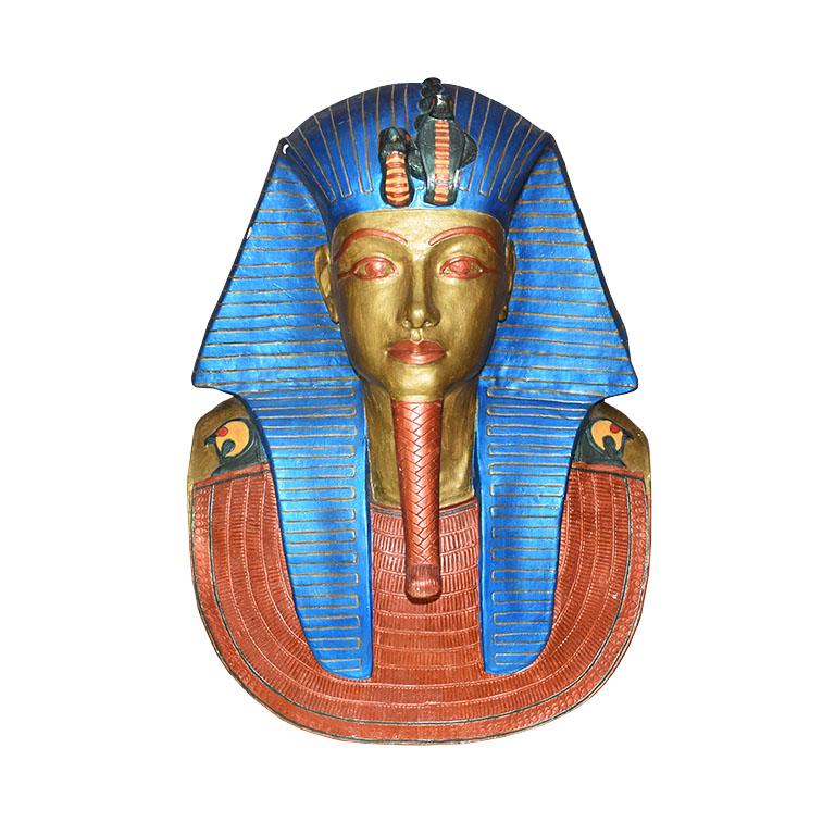 A handmade plaster but of the Egyptian King Tutankhamun. This lovely wall hanging will be an interesting addition to any space. It is created from plaster and hand-painted in metallic blues, deep reds, and golds. The piece depicts a 3 dimensional