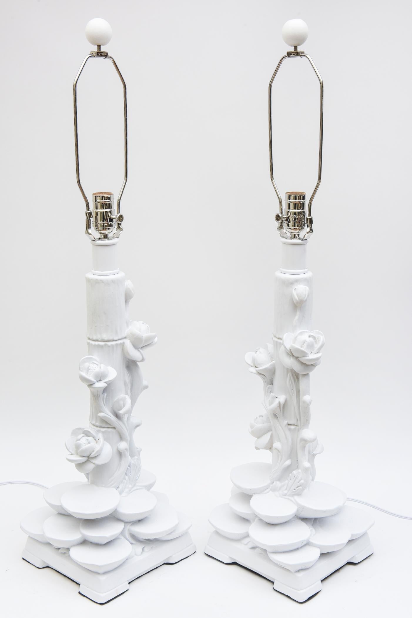 This beautiful pair of white restored Plaster of Paris table lamps are in the style of Serge Roche. The time period of these is Mid-Century Modern from the 60s. The subject matter are clusters of rows of lily pods at the base with vines of cascading