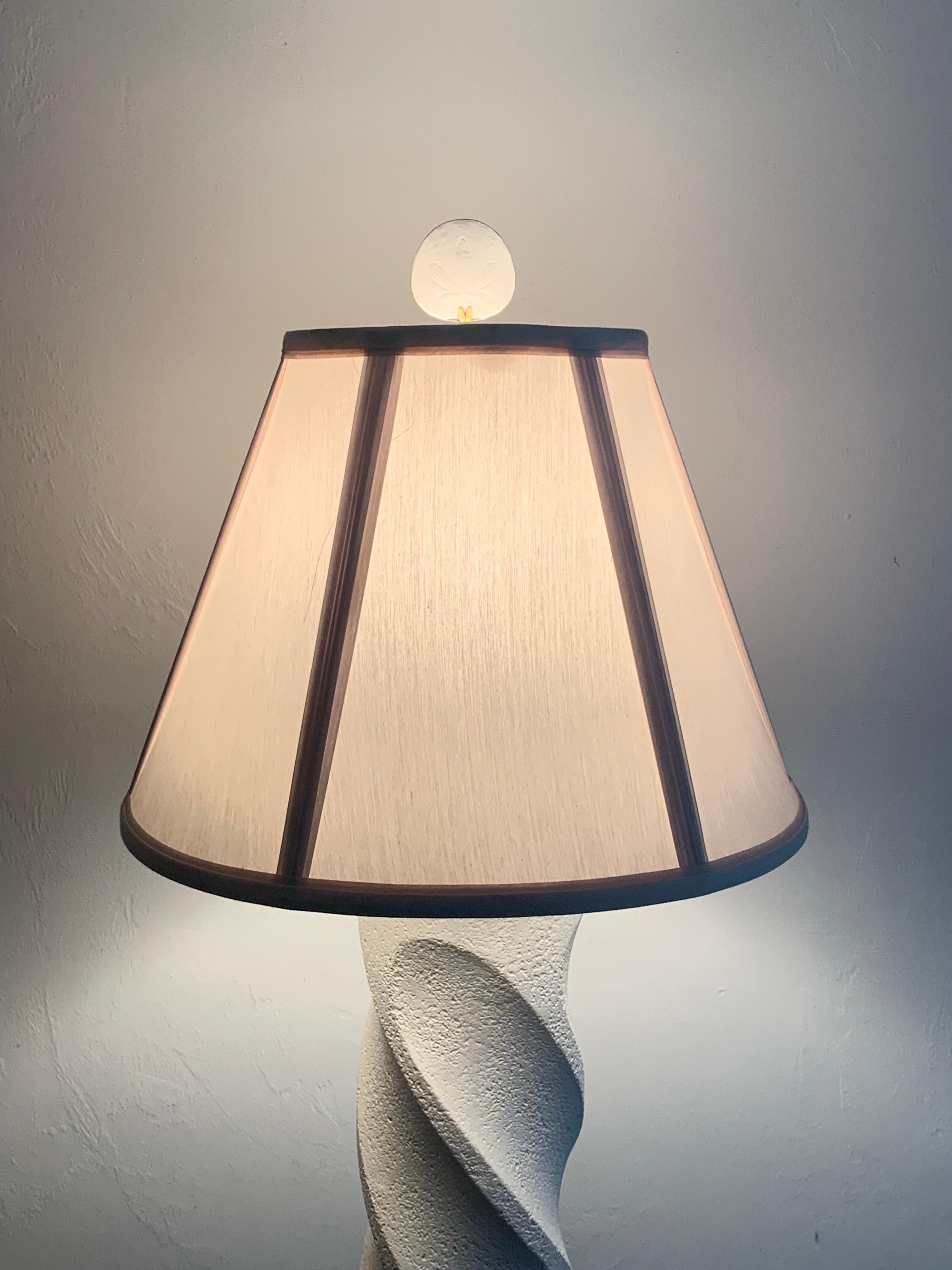 A plaster floor lamp in the style of Michael Taylor featuring a spiral column design with a circular base. The textured plaster offers an organic elegance reminiscent of white washed stone or unfilled travertine. Has a sand dollar finial. USA, 1990s.