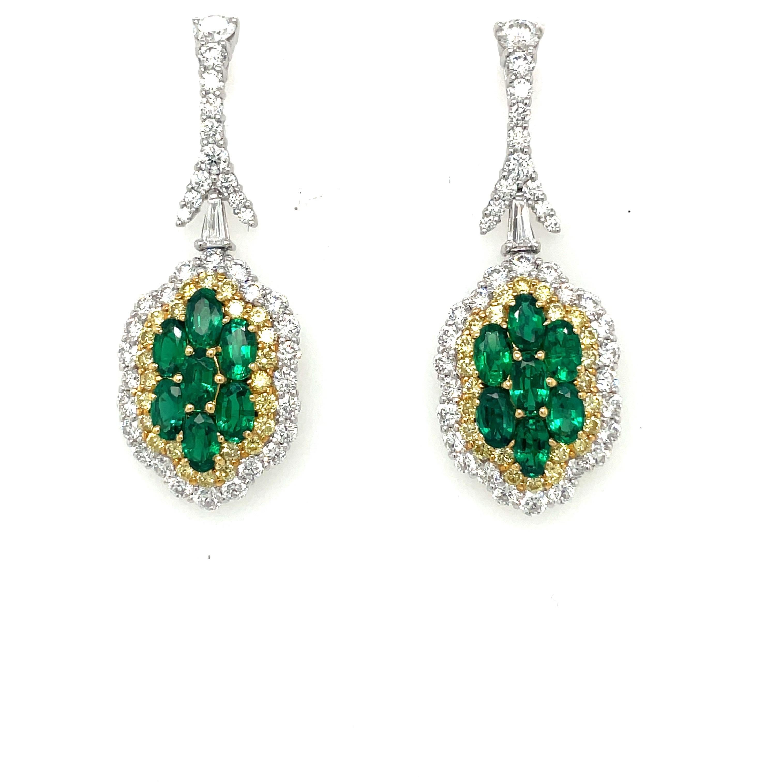 A magnificent pair of emerald and diamond hanging earrings. The platinum and 18 karat yellow gold earrings are set with a total of 14 oval emeralds. Natural yellow and white round diamonds surround the emeralds in a soft scalloped shape. The post