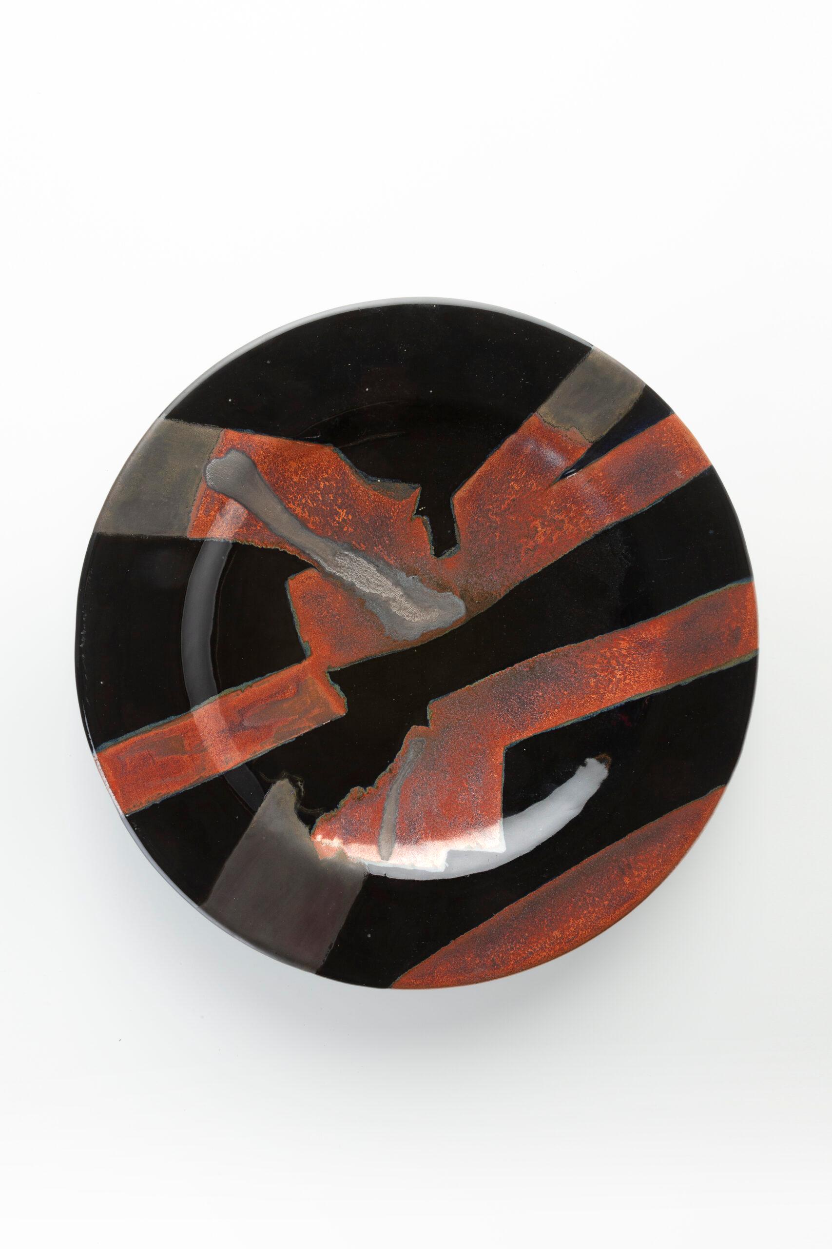 Questo piatto in ceramica di Jacques Pouchain mostra la sua caratteristica astrazione geometrica. Il fondo nero lucido è animato da audaci forme angolari rosso rame e grigie, che creano un sorprendente gioco di texture e contrasti. Funzionale e