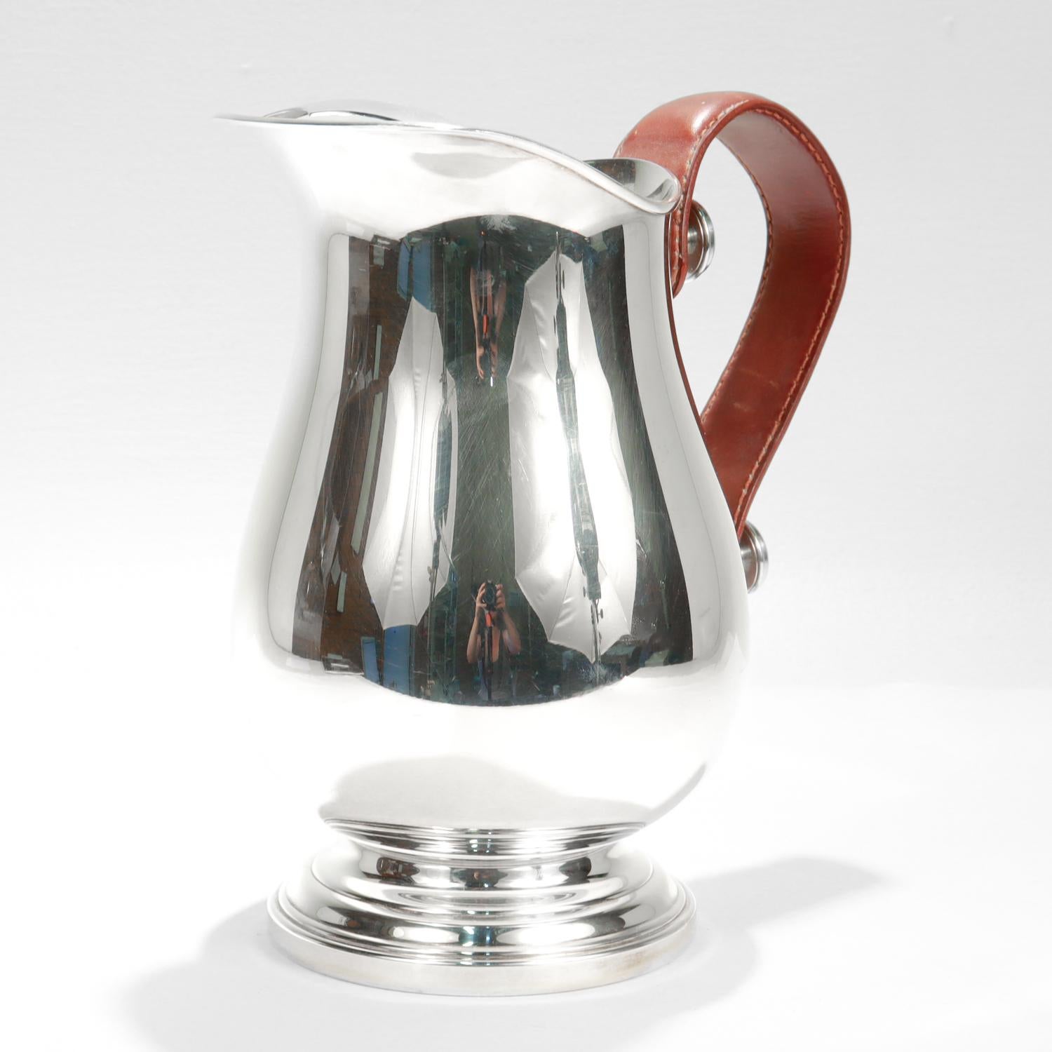 A fine modern water pitcher.

By Plata Lappas.

In silver plate.

With a c-shaped leather handel and strainer to the spout. 

Founded by Alcibiades Lappas 1887, Plata Lappas is a one of Argentina's highest-end puveyors of silver, silver plate and
