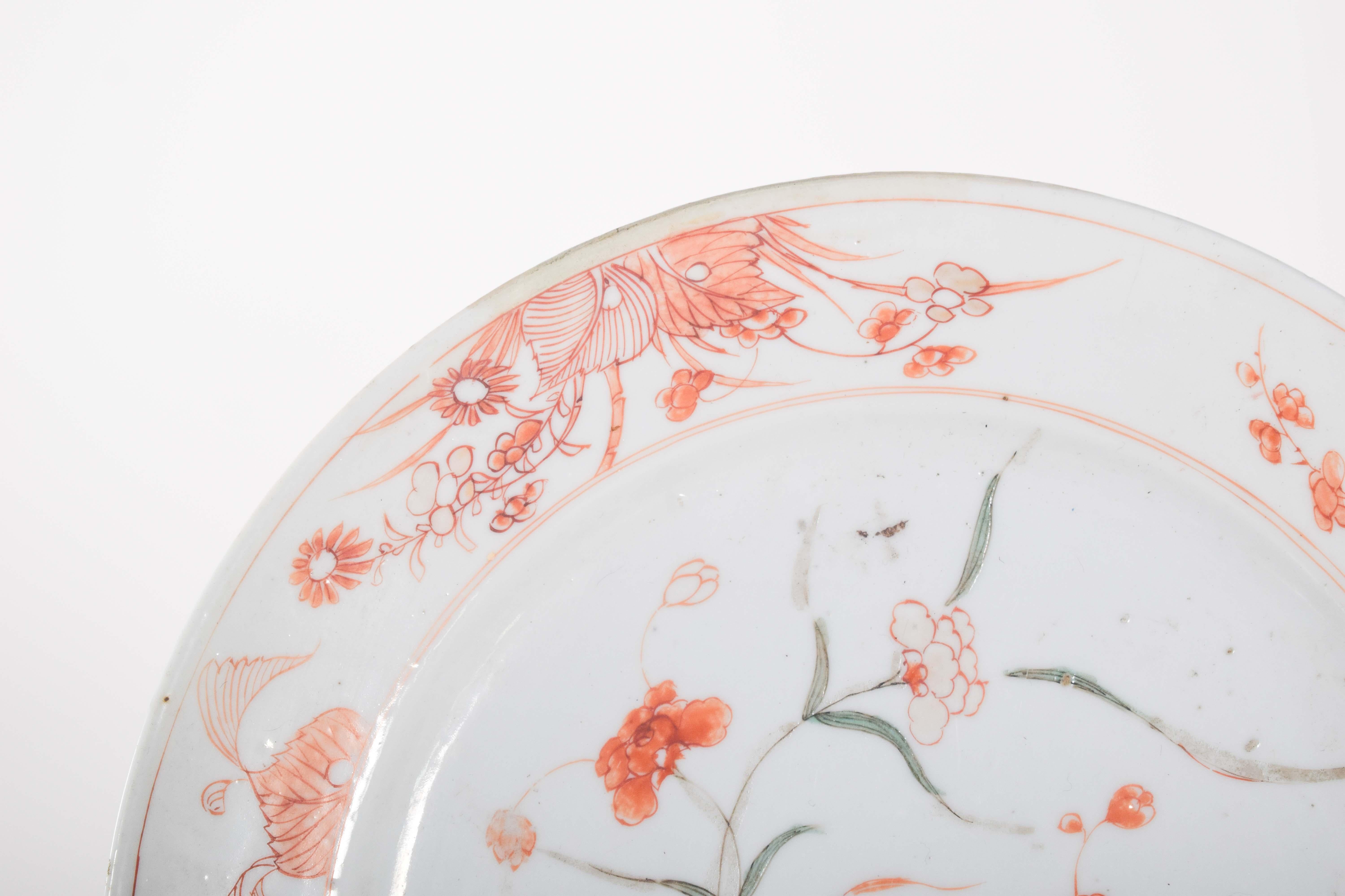 Plate, in Chinese export porcelain. Polychrome decoration, with floral motifs in shades of orange and green. The center of the plate features a cluster of stylized flowers, with rouge de fer petals and green leaves, complemented by fine black