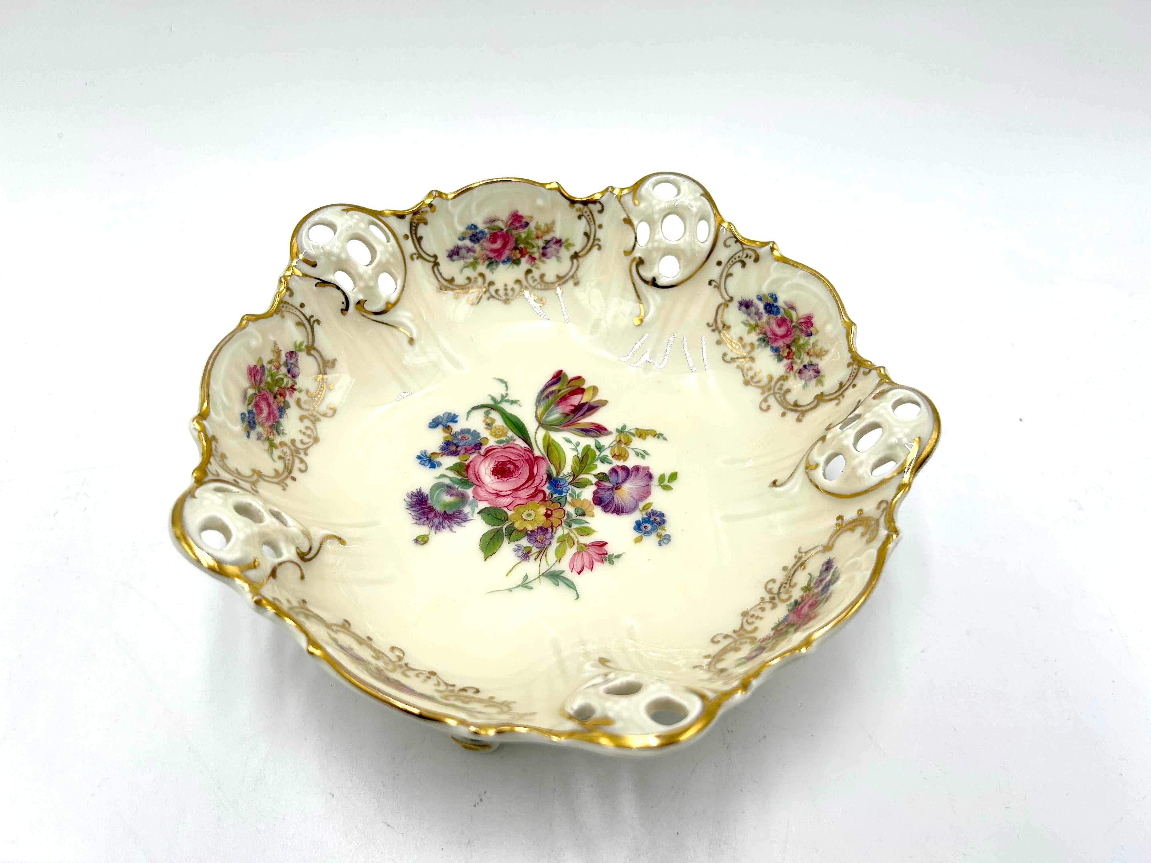 Openwork plate supported on three filigree legs from the Moliere collection, the renowned German Rosenthal label. The product is marked with the mark used in 1957. Ecru porcelain decorated with openwork sides, floral bouquets and gilded