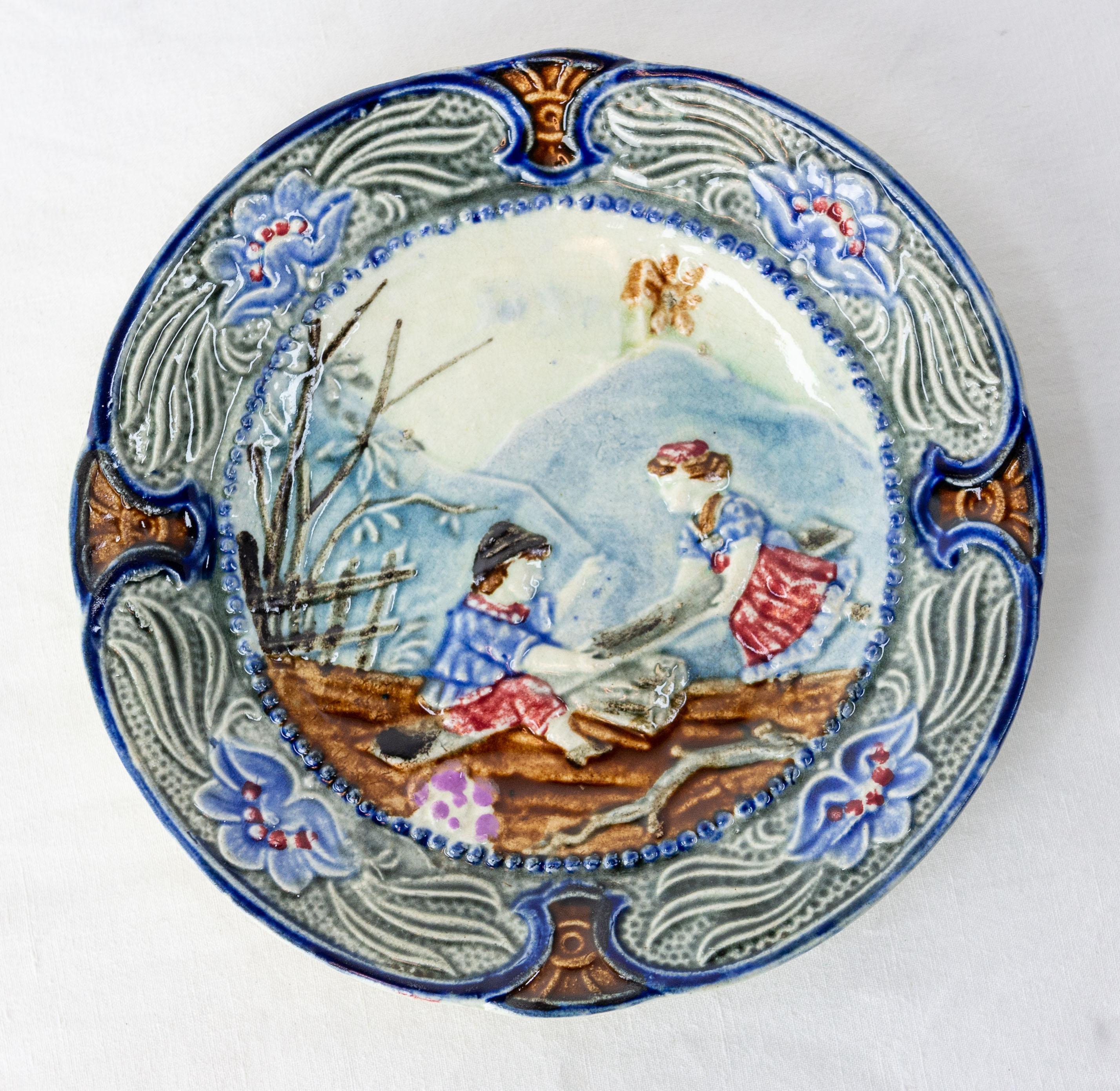 Belgium plate, made in the manufacture of Wasmuel in Belgium in the late 19th century.
This manufacture was known of its speciality of barbotines. It was opened between mid 19 th century and mid 20th century.

This naive scene represents a boy and a