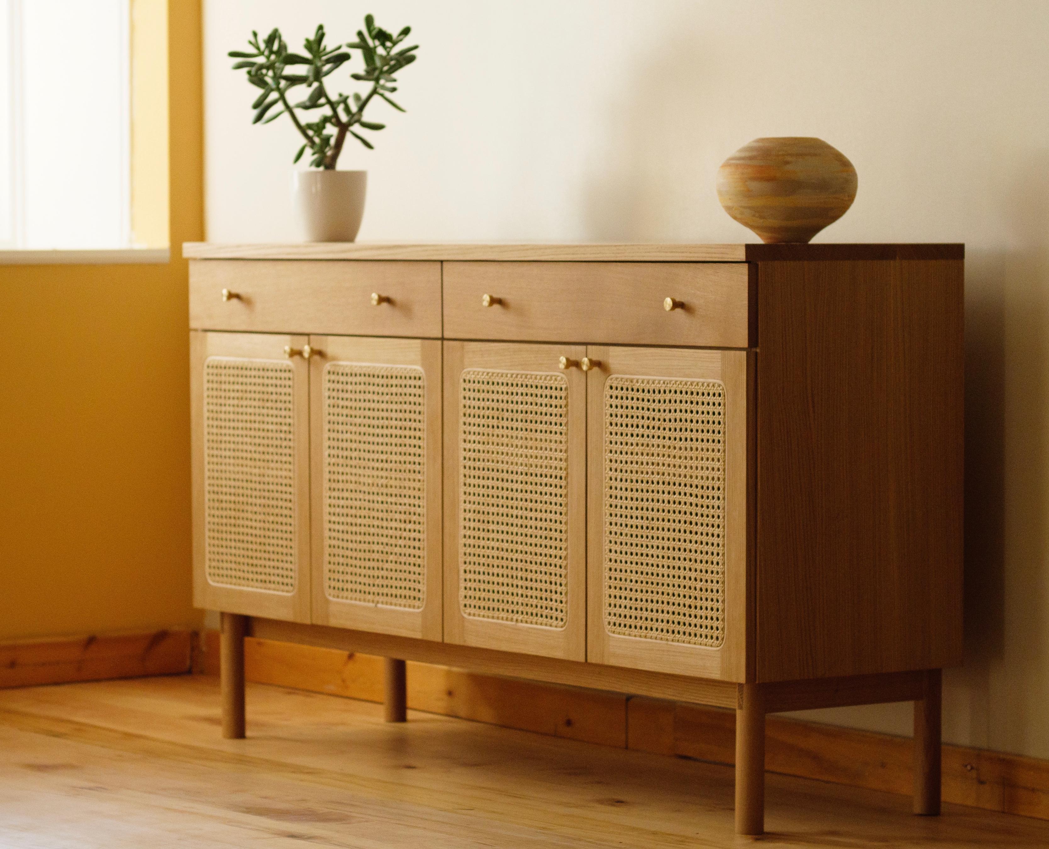 La credenza Plateau è un mobile in legno massiccio realizzato con tiretti in ottone, guide per cassetti con chiusura ammortizzata e cerniere per ante con chiusura ammortizzata. Il mobile presenta ante con inserti in rattan naturale in una struttura