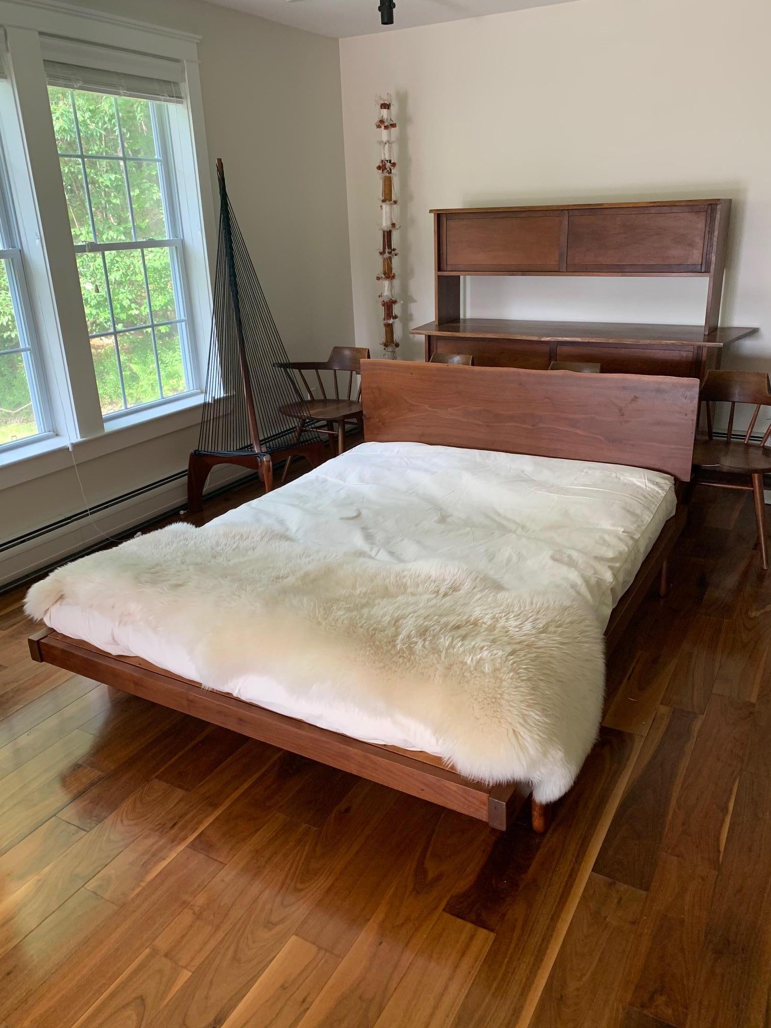 Platform bed studio crafted in the style of George Nakashima circa 1960s. It features a mounted walnut slab headboard that display free edge on top. The slab itself is 16.5 inches in height. The bed is supported by four feet with typical wood