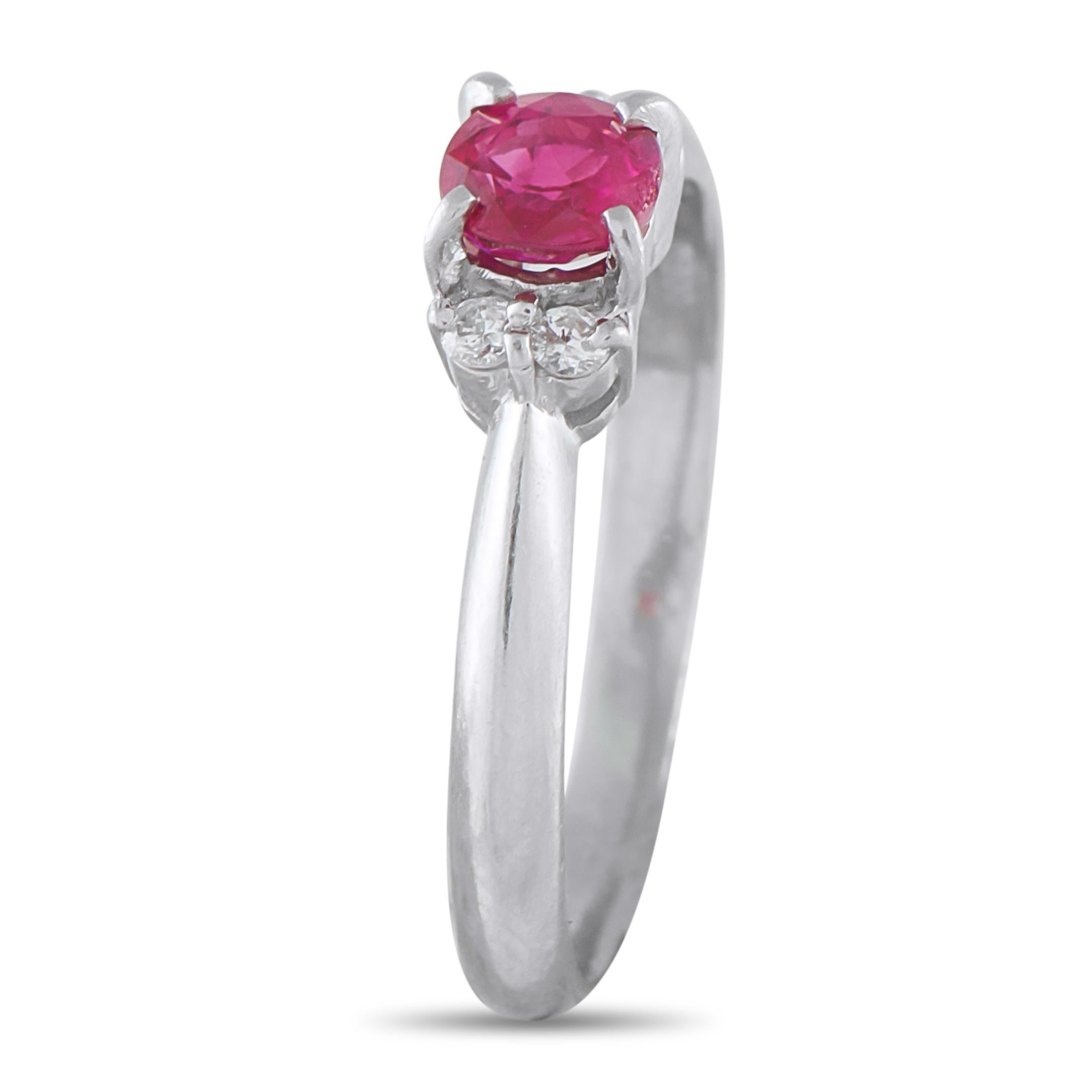 This ring focuses the eye on a single round ruby held securely aloft by elegant claw prongs. Flanking the colored central gem are brilliant duos of round diamonds on each side, creating a balanced setting. The precious stones sit atop a sleek