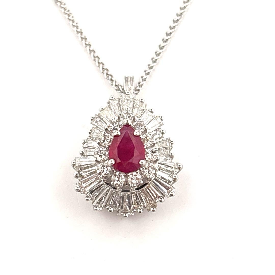 Ce bijou vintage saisissant sert à la fois de bague et de pendentif, offrant une polyvalence et une élégance intemporelle. 
En son centre se trouve un rubis poire richement coloré, encadré par un halo de diamants ronds de taille brillant et par un