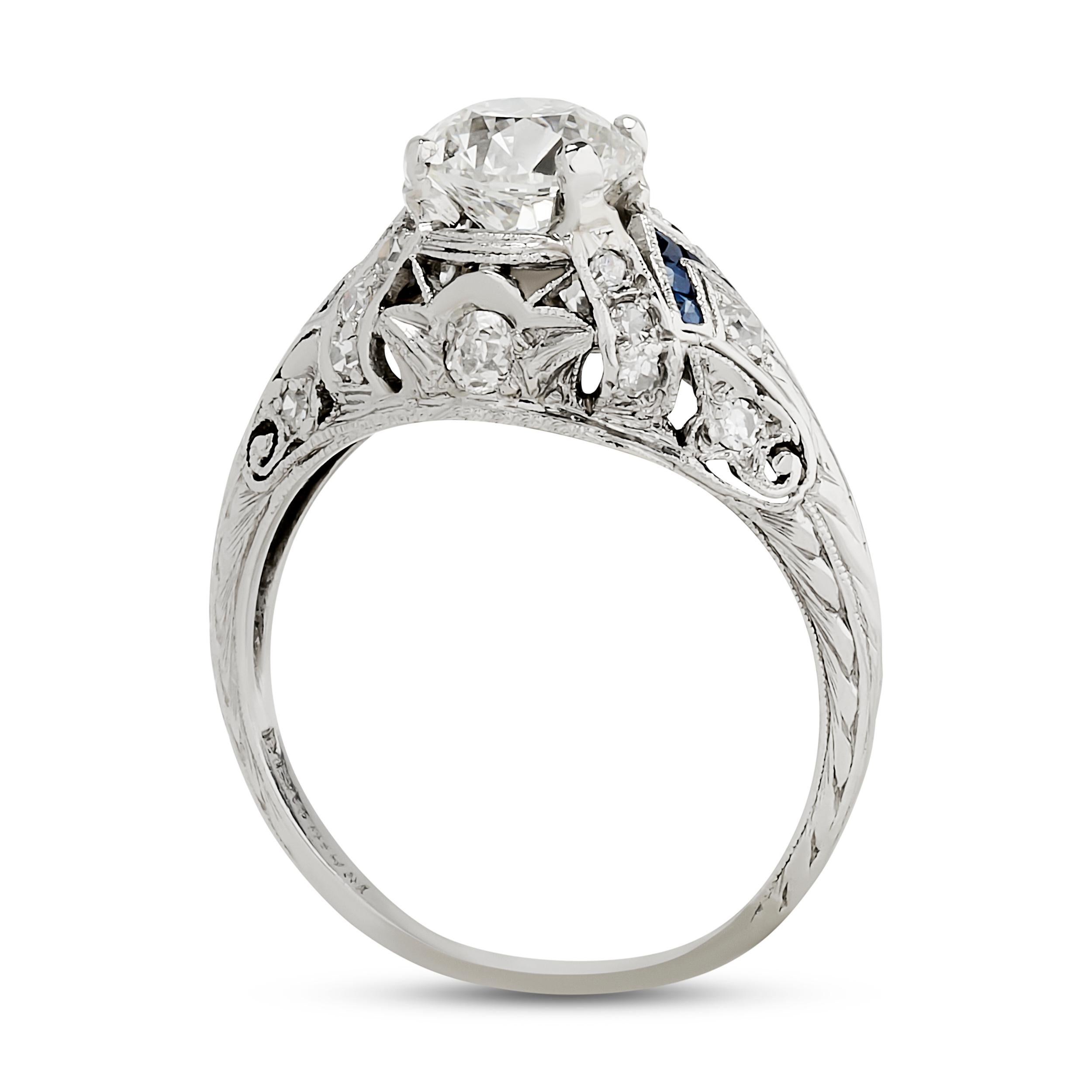 This platinum ring features a round brilliant diamond set within a geometric, octagonal frame, accented with channel-set blue sapphires and smaller diamonds, all crafted with intricate milgrain detailing and hand-engraved motifs.

Center Round