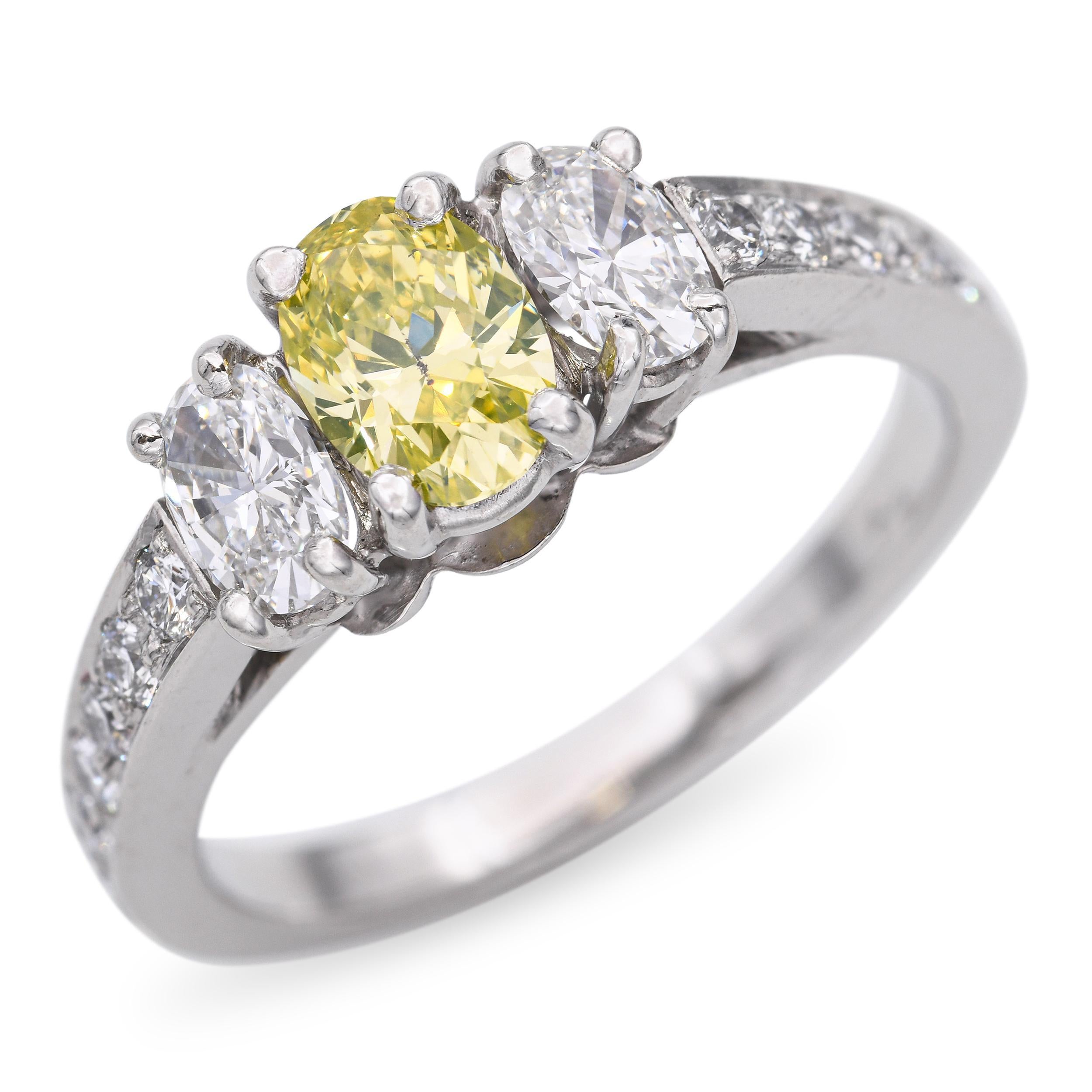 Bague vintage en platine à trois pierres mettant en valeur un diamant captivant de couleur jaune verdâtre au centre, flanqué de deux diamants blancs. La monture en platine aux lignes épurées rehausse le contraste entre la chaude teinte vert doré de