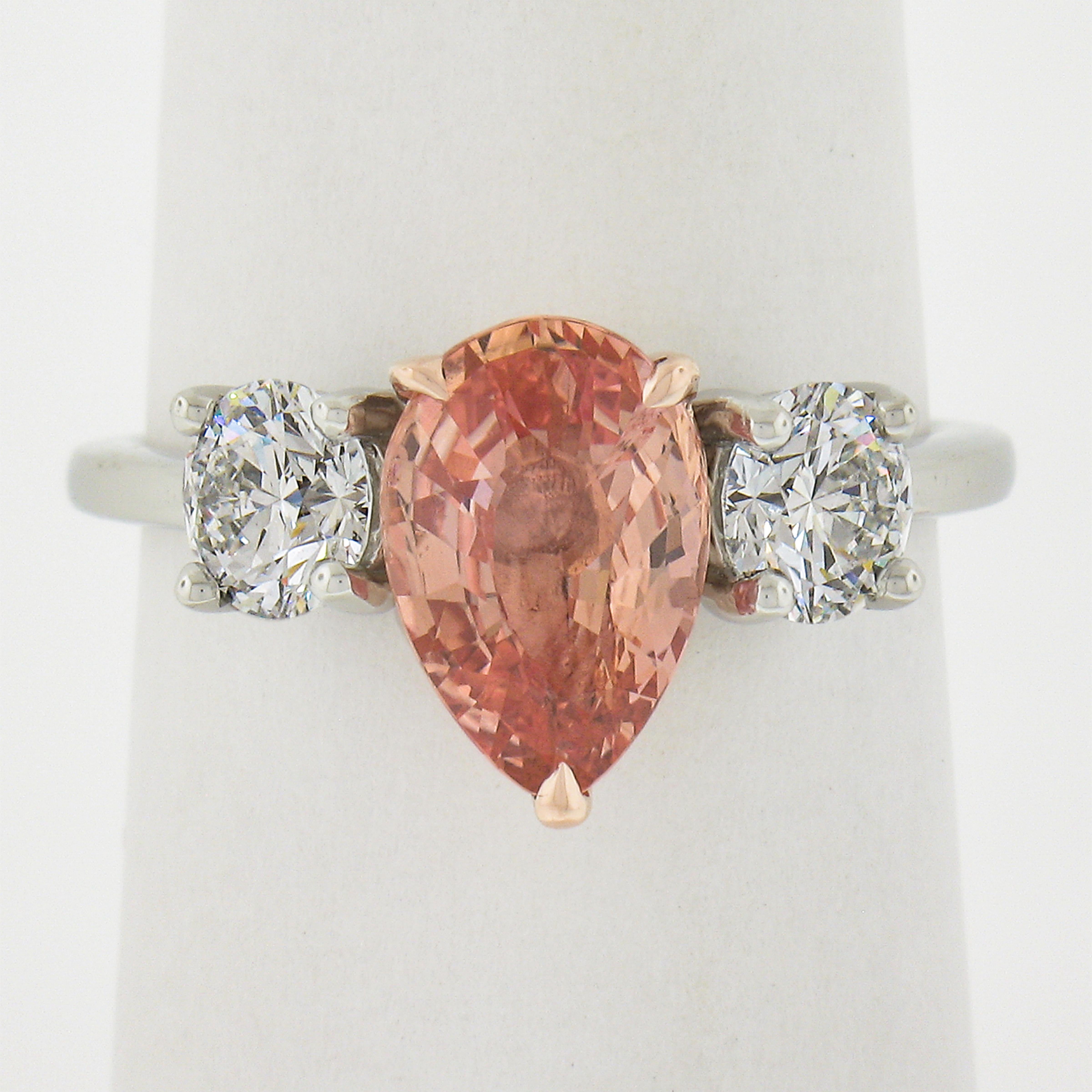 This very elegant and chic padparadscha sapphire and diamond three stone engagement ring is custom designed and crafted in solid platinum. It features a fiery, GIA certified pinkish orange Ceylon sapphire stone that is neatly set in the 14k rose