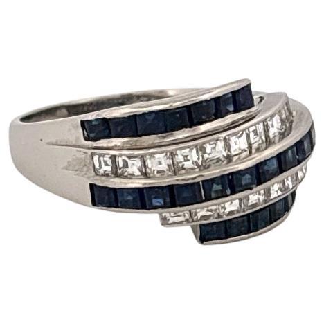 Questo anello in platino presenta uno straordinario spettacolo di eleganza e raffinatezza, con 1,74 carati di zaffiri blu intenso e 0,82 carati di diamanti a taglio quadrato. Il design mette in mostra tre file graziosamente curve che si intrecciano,