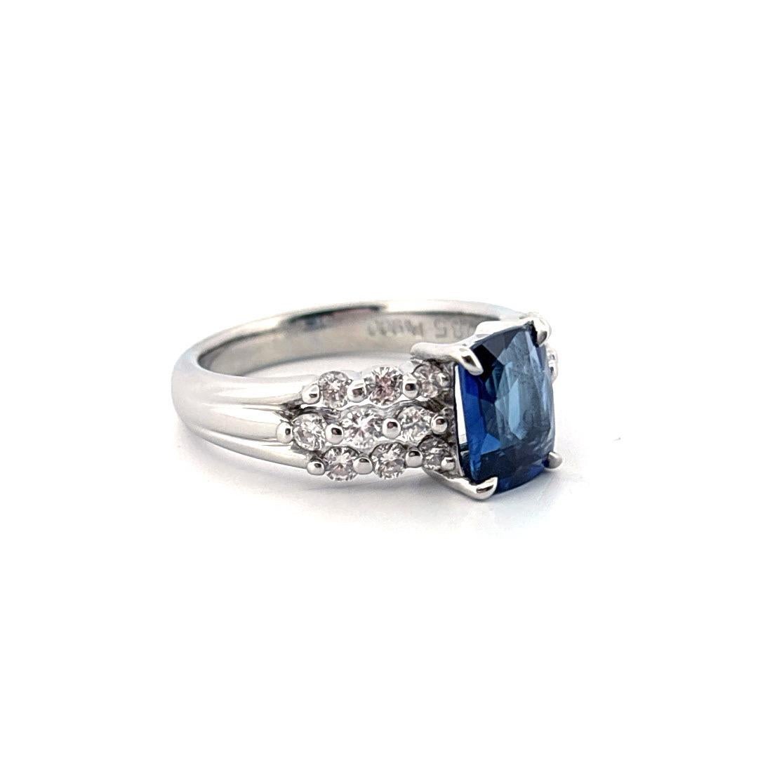 Dieser Platinring strahlt zeitlose Eleganz aus und präsentiert einen blauen Saphir im Kissenschliff mit einem Gewicht von 1,85 Karat als lebhaftes Herzstück. Der samtige, königsblaue Farbton des Saphirs wird durch ein Trio von diamantbesetzten