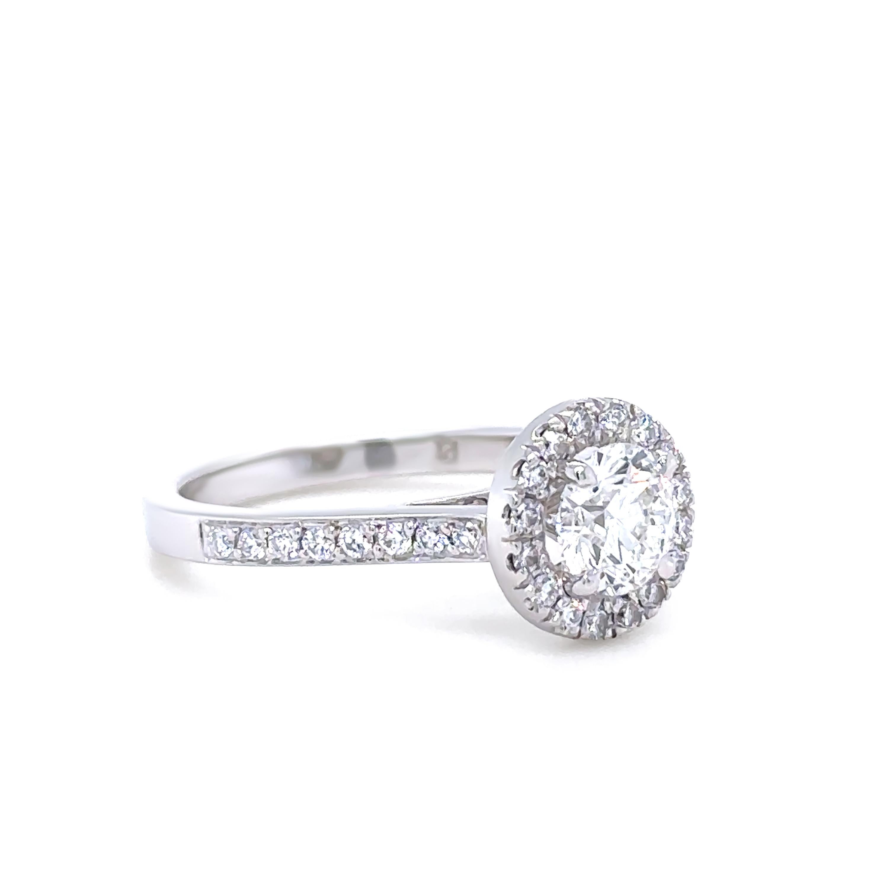 This elegant bridal set features a cast platinum engagement ring with a central 0.80ct round brilliant-cut diamond of H colour and SI1 clarity, surrounded by a halo of sixteen 0.01ct diamonds and accented by sixteen additional diamonds along the