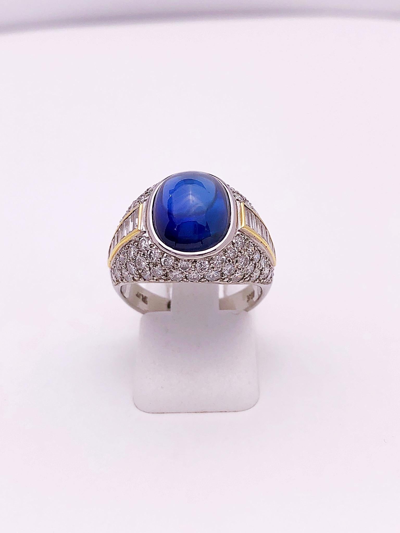 A lovely classic style platinum ring centering a 6.84 carat oval cabochon blue sapphire. This domed ring is pave set with round brilliant diamonds . A single row of diamond baguettes set in 18 karat yellow gold accent the center of the ring. Total