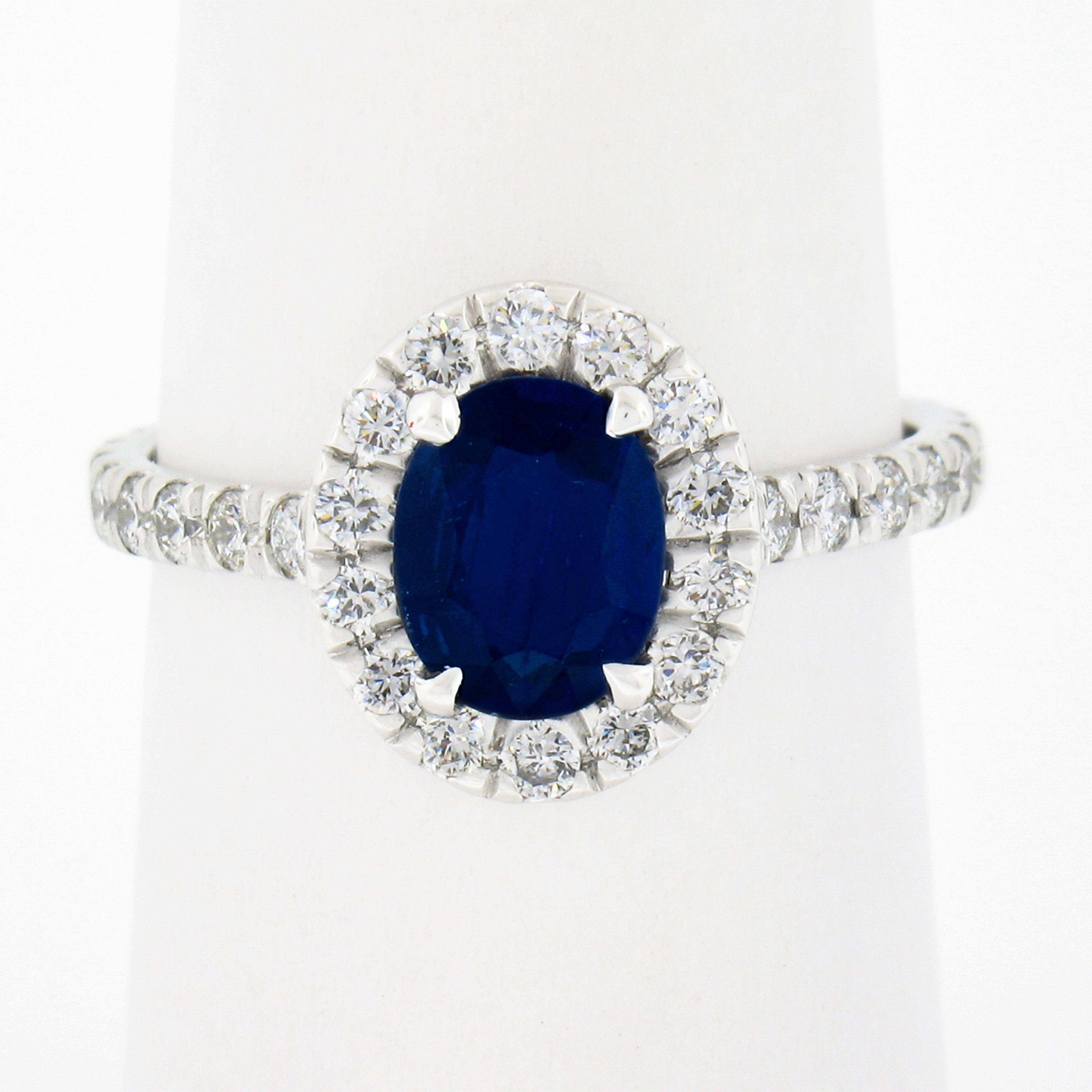This chic and well made sapphire and diamond engagement ring is newly crafted in solid platinum. It features a vivid oval blue sapphire that is elegantly claw-prong set at the center of a diamond halo design. The fine quality solitaire weighs 1.10