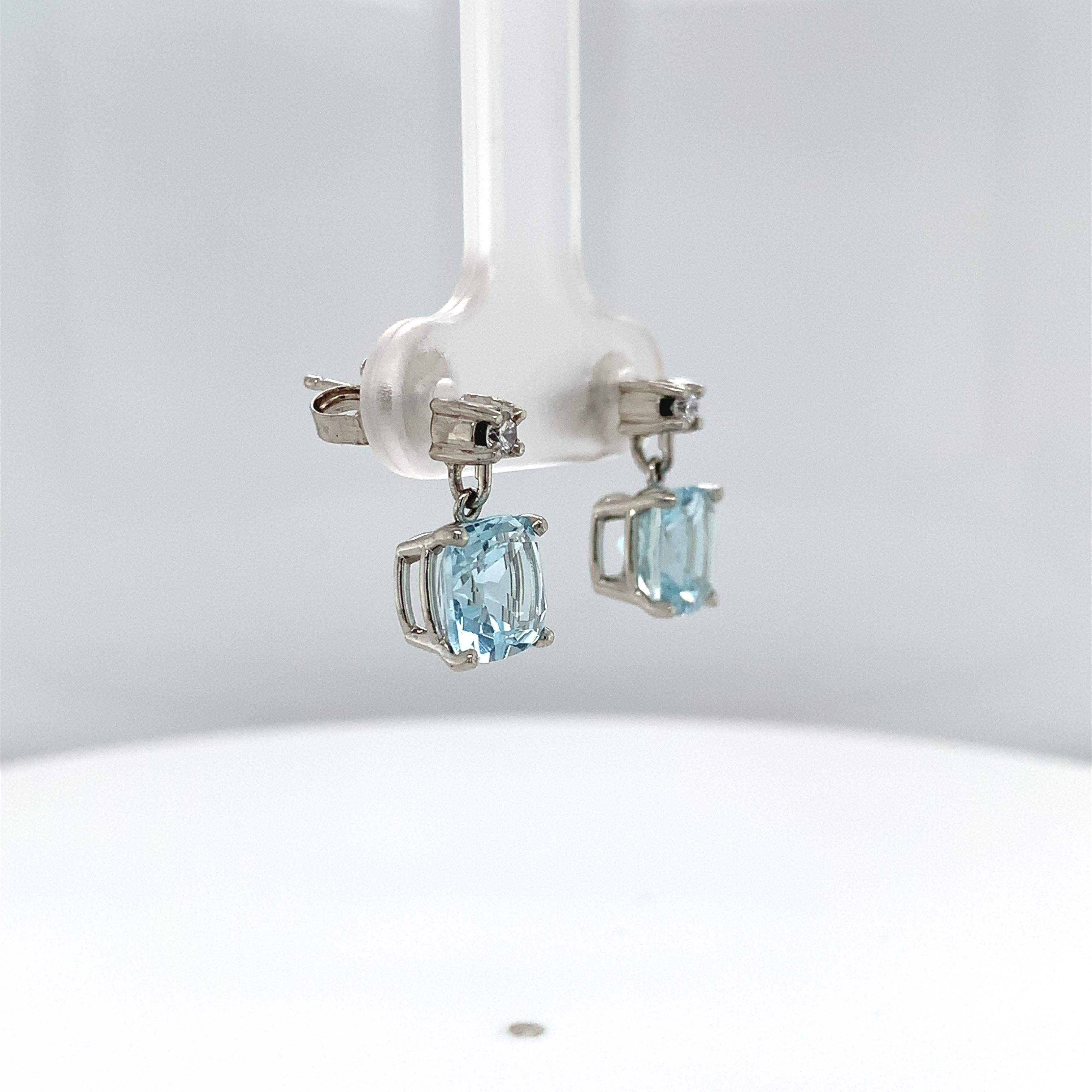 Platinum aquamarine and diamond dangle drop earrings. The cushion cut light blue aquamarines measure about 7mm and weigh 2.85 carats total. There are 2 small round diamond accents measuring about 2mm. The earrings are post with friction backs. They