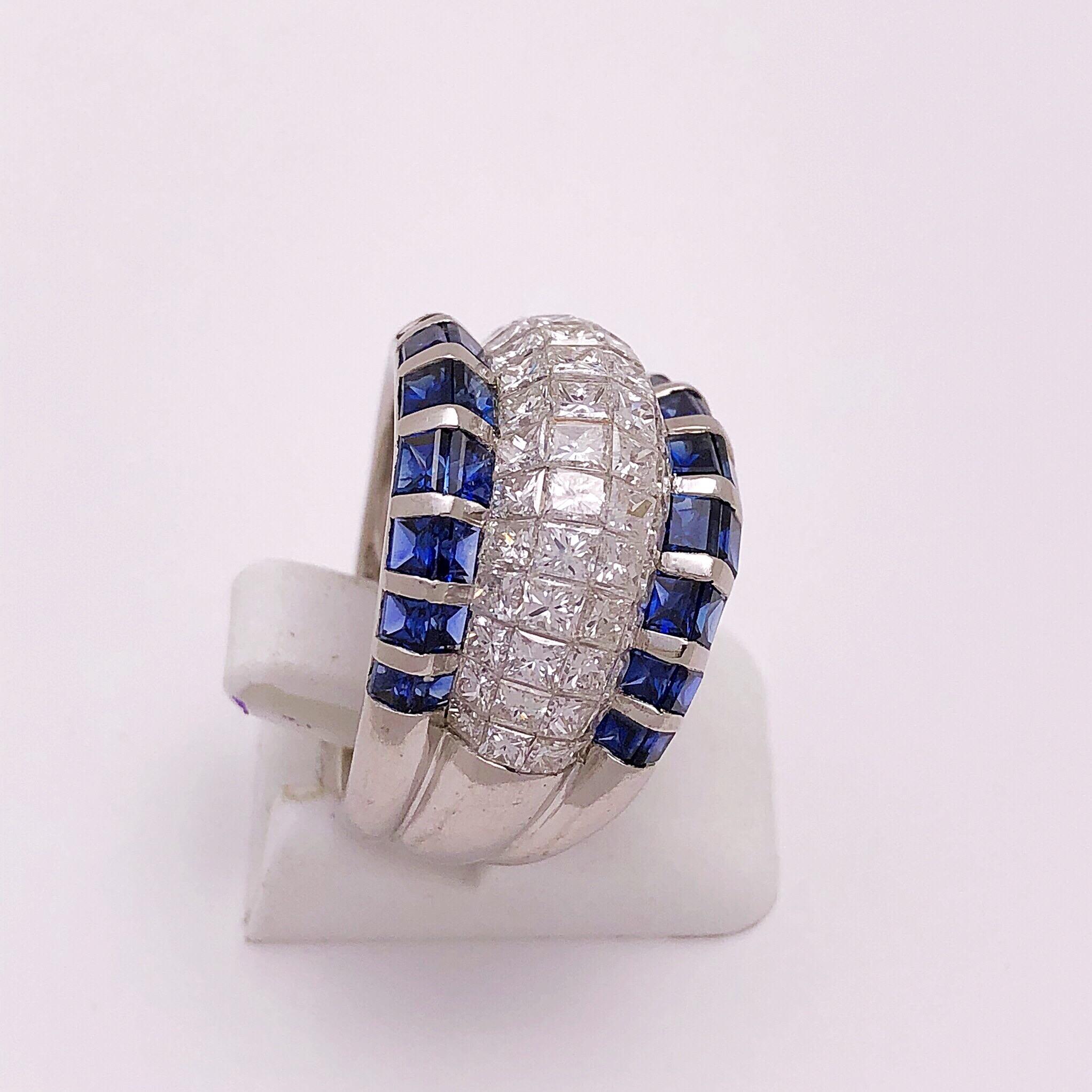 This elegant platinum ring centers four rows of invisibly set Princess cut diamonds.The diamonds are bordered on each side by two rows of Princess cut blue sapphires. Also invisibly set in a precise setting so that the two rows form an angled