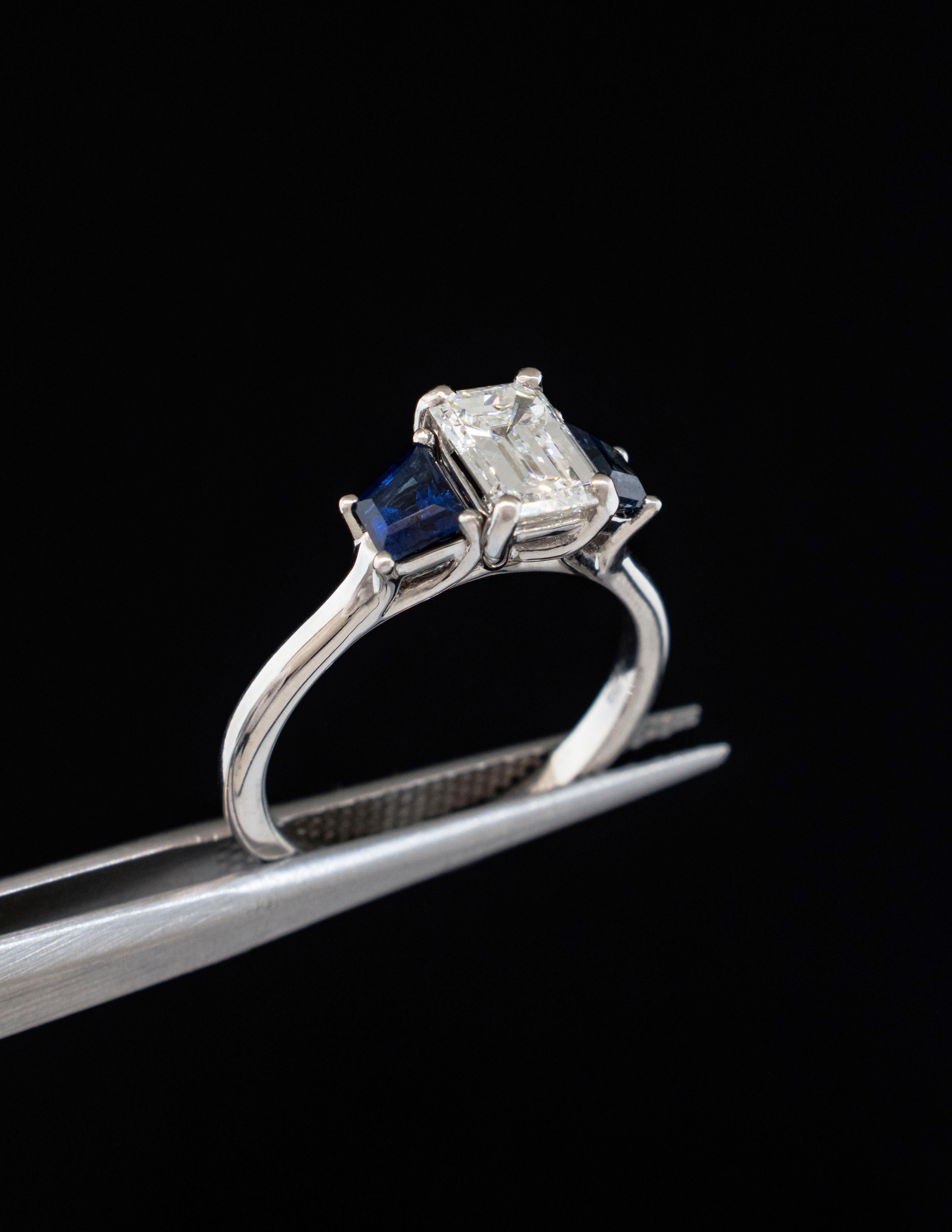 Bague classique en platine à trois pierres, diamant et saphir.
Le diamant central de taille émeraude pèse environ 1,20 carat et présente une pureté VVS2 et une couleur G. Les diamants taille émeraude présentent toutes les inclusions et la pureté VVS