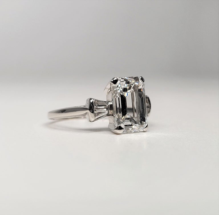 This beauty is in a lovely platinum mounting, stamped Orange Blossom, centered with one prong-set, emerald-cut diamond, flanked by four channel-set, tapered baguette-cut diamonds. 

The diamond is accompanied by GIA report # 2225374056, which states