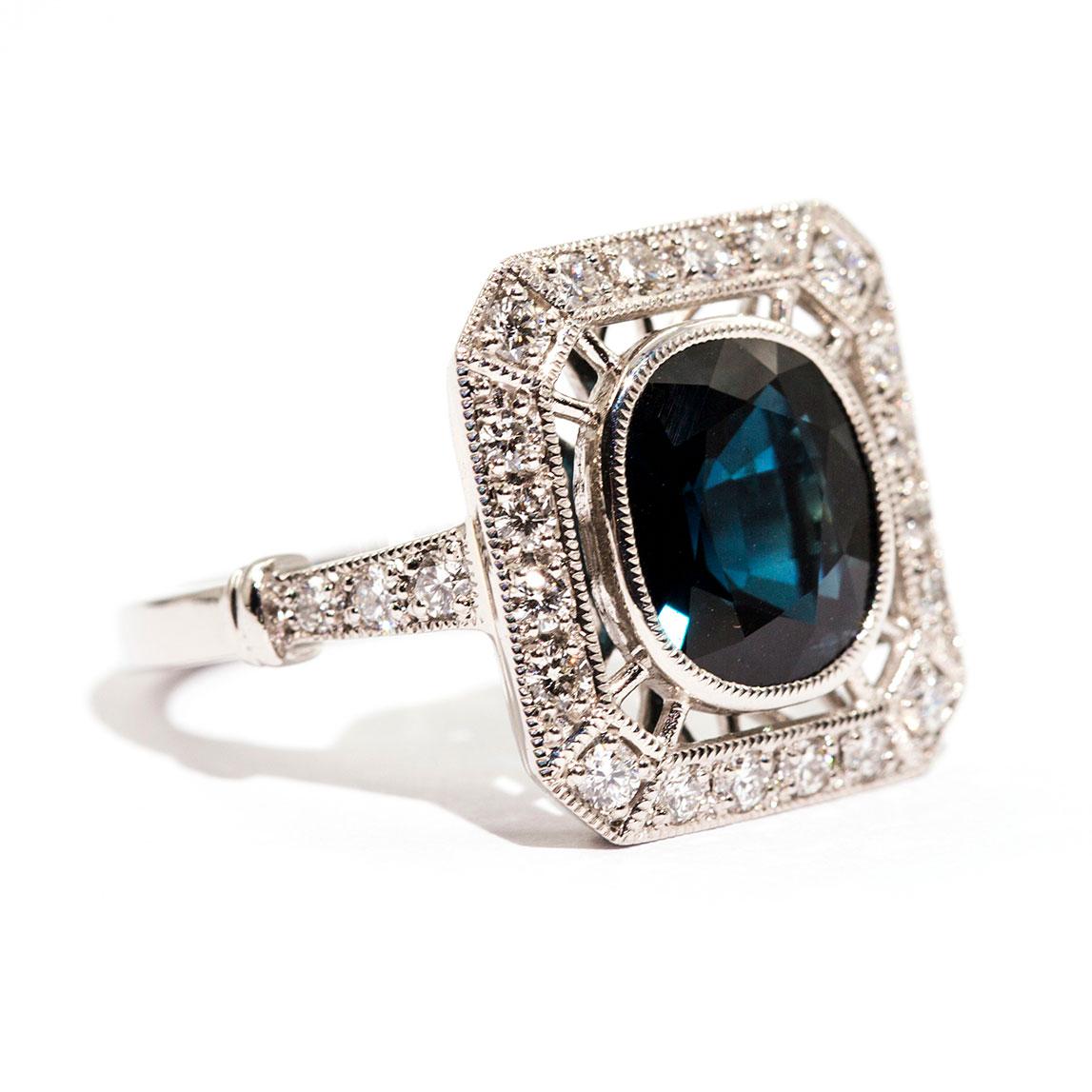Forged in platinum, this fabulous art deco inspired ring features an enchanting 3.97 carat cushion cut natural deep blue sapphire. This spectacular gem is encompassed by 0.64 carats of radiant round brilliant cut diamonds. We have named this
