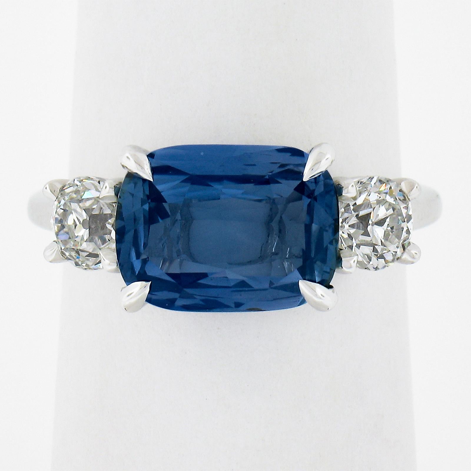 This gorgeous, custom designed, sapphire and diamond ring features a truly breathtaking, GIA certified, cushion cut old sapphire solitaire that is perfectly claw prong set at its center and flanked by two fine quality old European cut diamonds. The