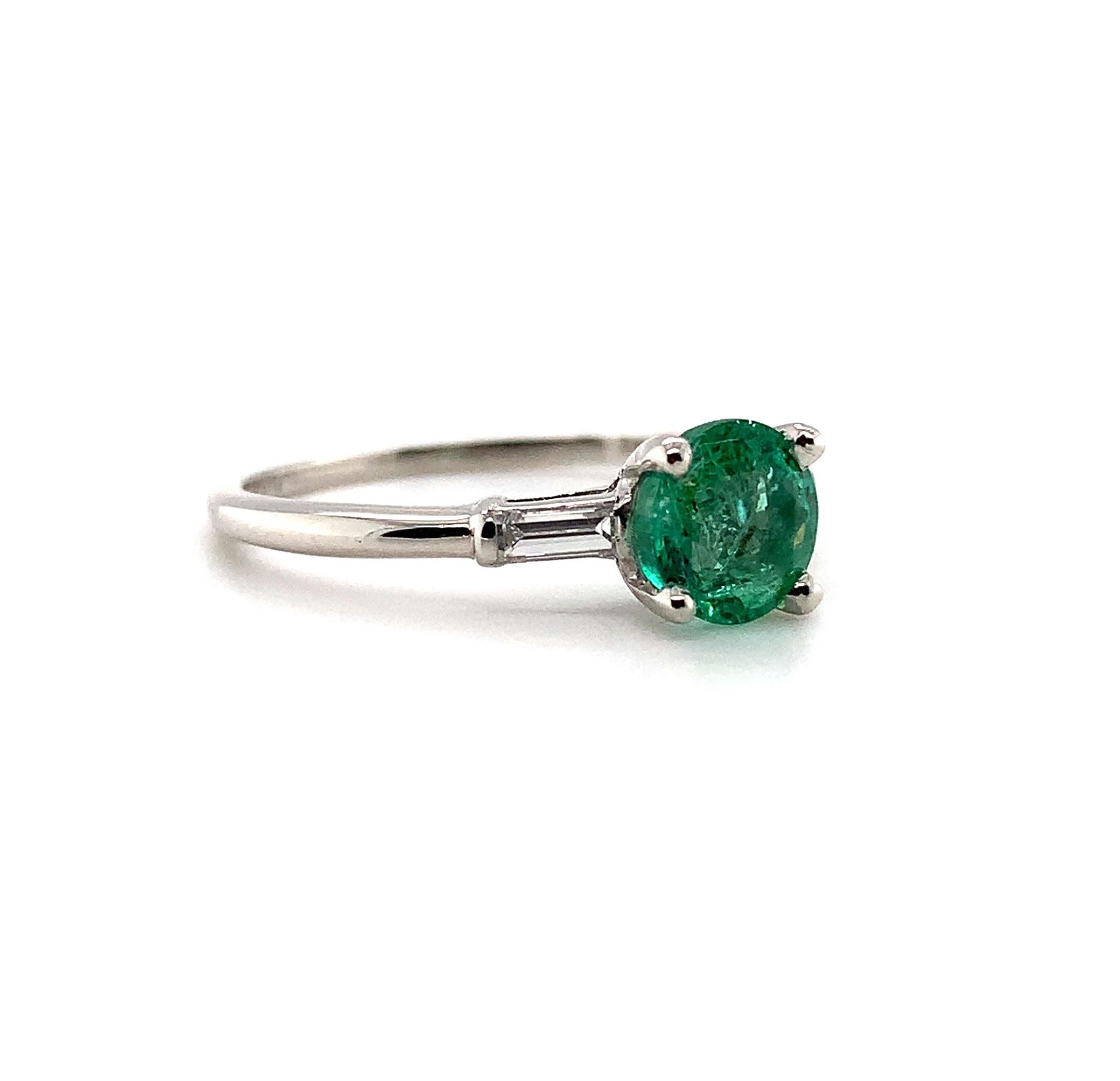 Platinum emerald and diamond ring featuring a round emerald weighing .83cts. The emerald has crisp mint green color and fine clarity. It measures about 6 mm. The emerald is accented by 2 baguette diamonds measuring about 3.5mm x 1.7mm and weighing