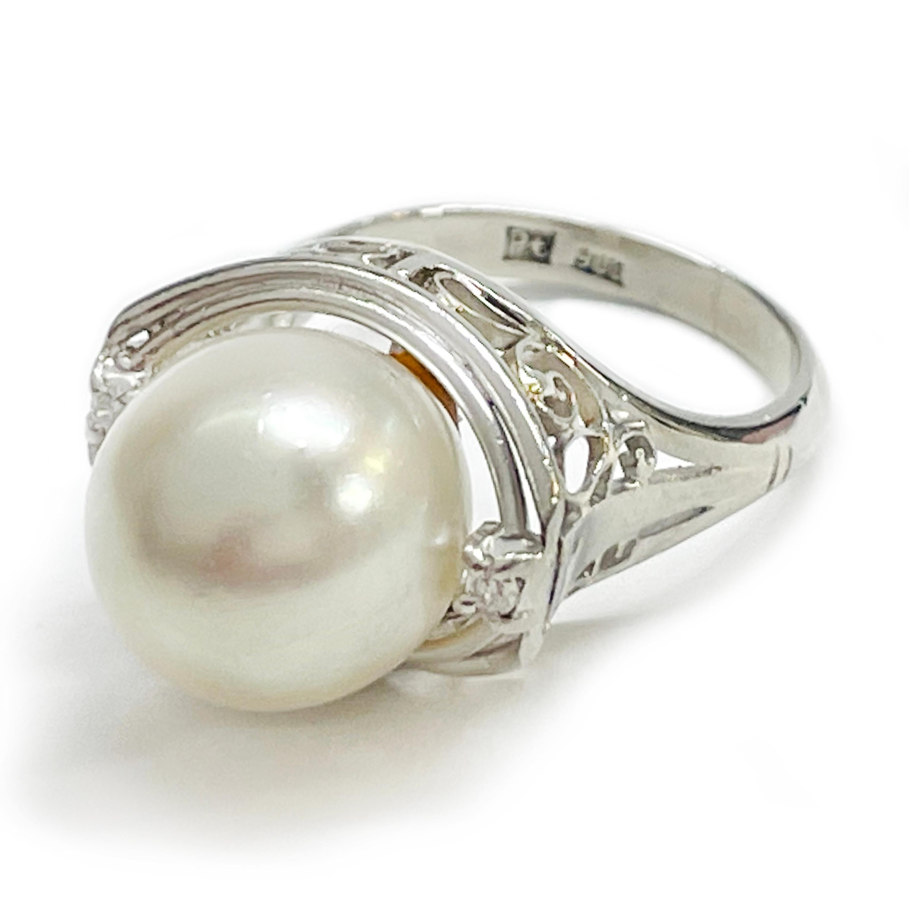 Platinum Pearl Diamond Ring. The ring features a 10mm white Ayoka center pearl flanked by a round melee diamond prong-set on each side. The pearl is white and cream with good luster. The diamonds have a total carat weight of 0.03ct. The ring has a