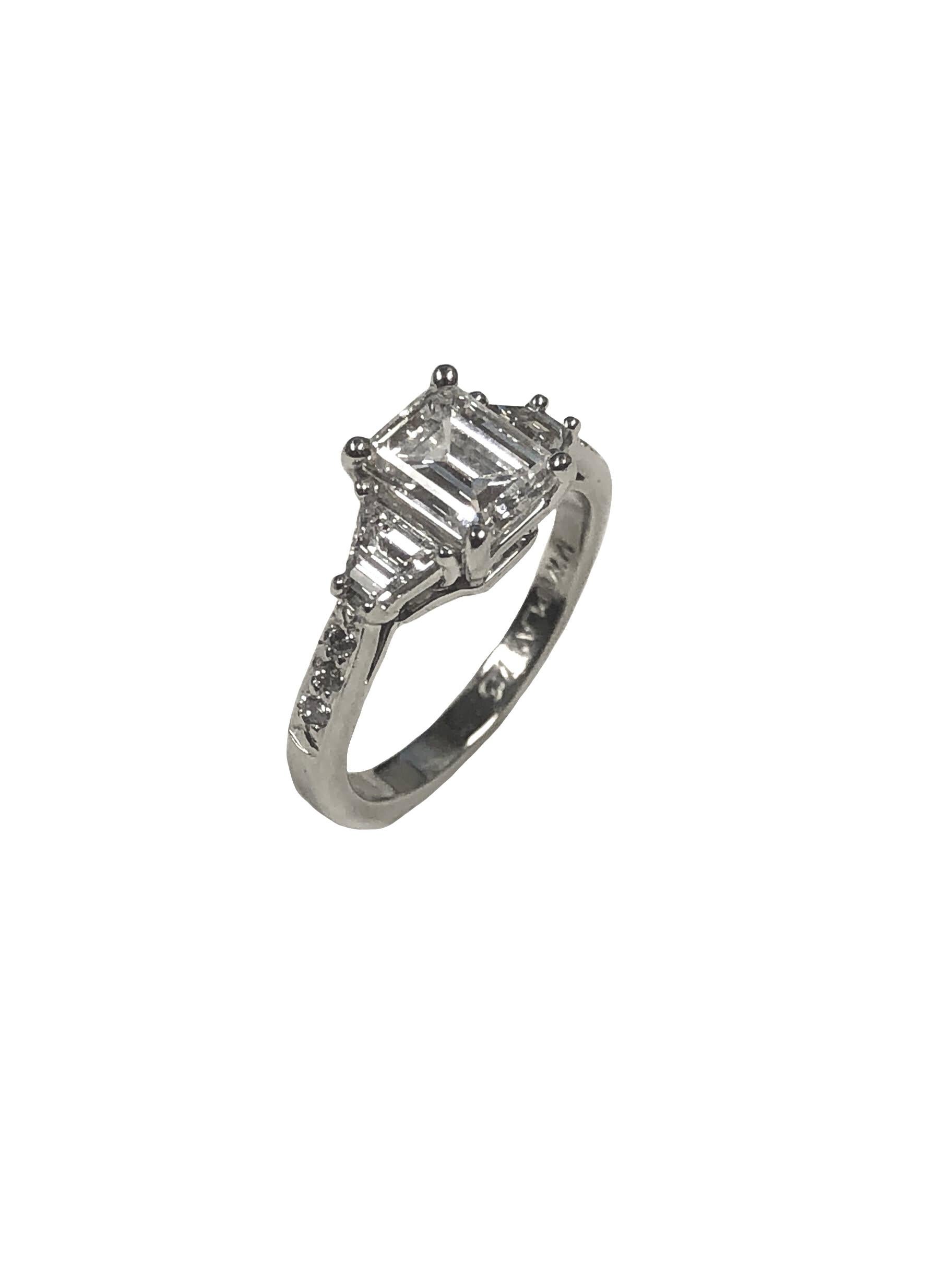 Circa 2000 Platinum Engagement Ring, centrally set with a Step cut, Emerald cut Diamond weighing 1 Carat and Grading as H in color and VS in clarity, further set on either side with  Trapezoid Diamonds and  round Brilliant cut Diamonds totaling