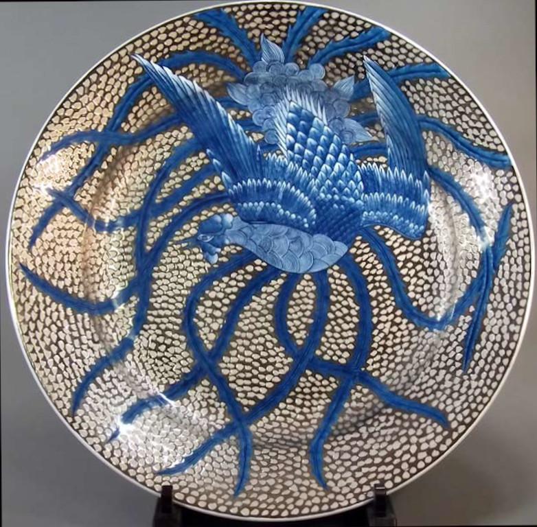 Exquisite dimpled Japanese decorative porcelain charger intricately hand painted, showcasing a dramatic breathtaking phoenix in deep blue extending its beautiful long wings to cover the entire body of the vase, set against a stunning platinum
