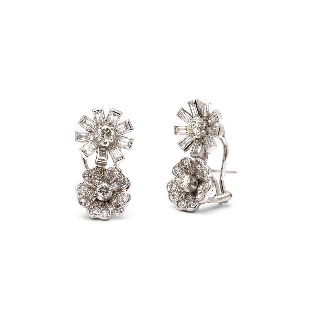 A stunning pair of stud earrings crafted in platinum. The unique floral design features one flower comprised of emerald cut diamonds with a round diamond center sitting atop another flower with heart-shaped petals pave set with round brilliant cut
