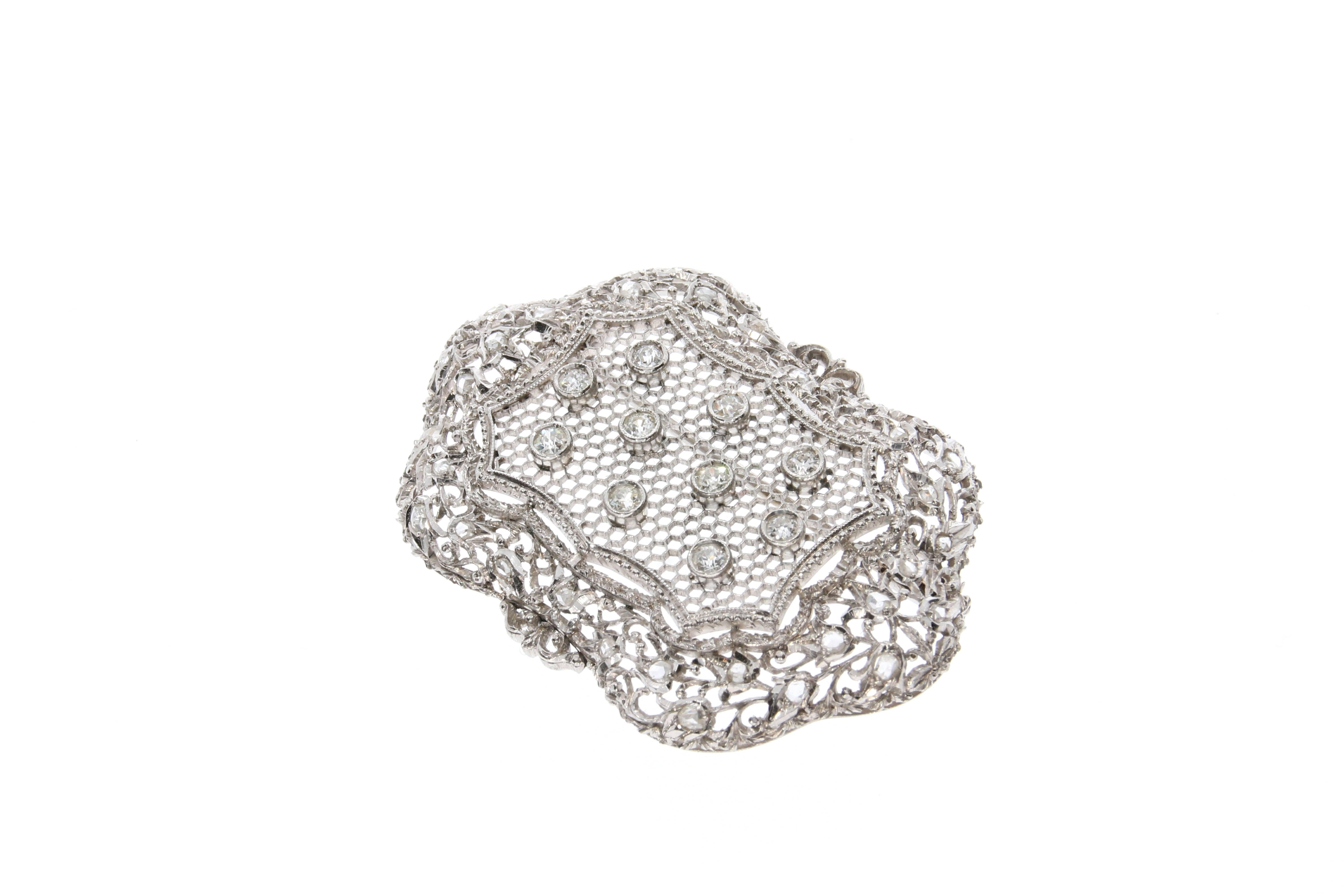 An antique platinum and diamond brooch. The intricate diamond set filigree frame is centered with a honeycomb net featuring ten diamonds weighing approximately 0.65 carats in total. The frame is decorated with small rose-cut diamonds weighing